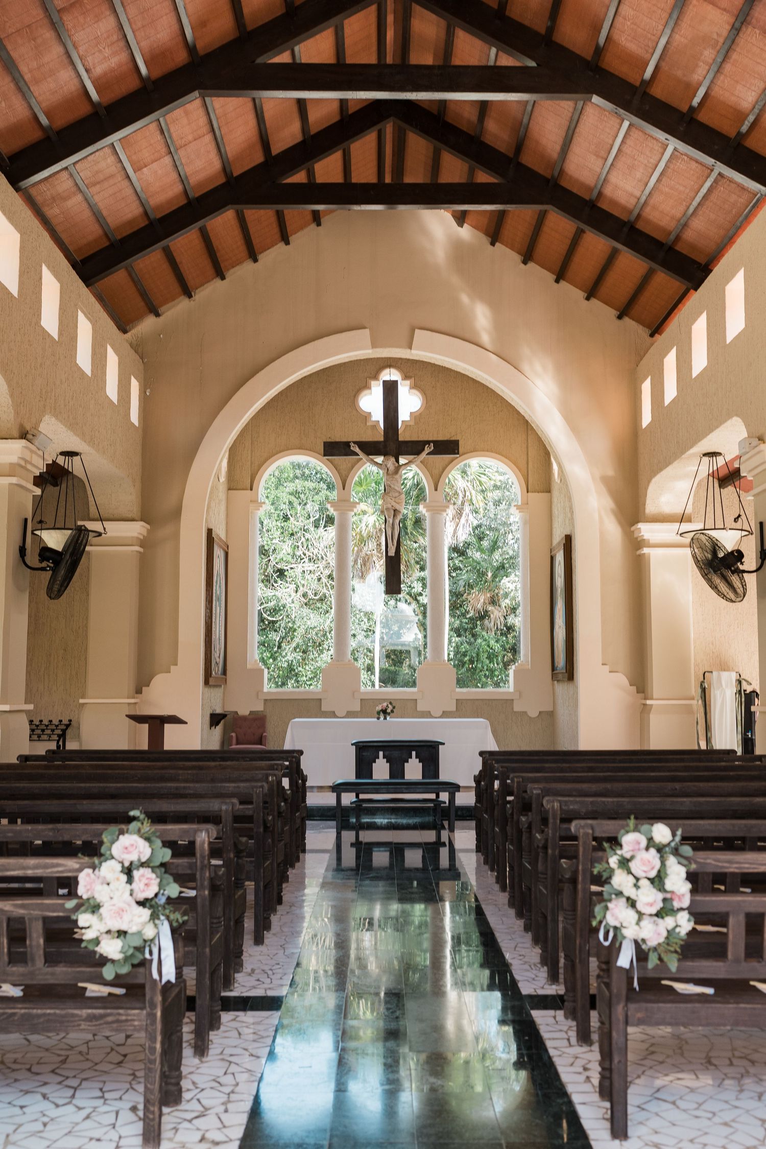 Elegant chapel interior with wooden pews, floral arrangements, cross above altar, and vaulted ceiling for a wedding ceremony.