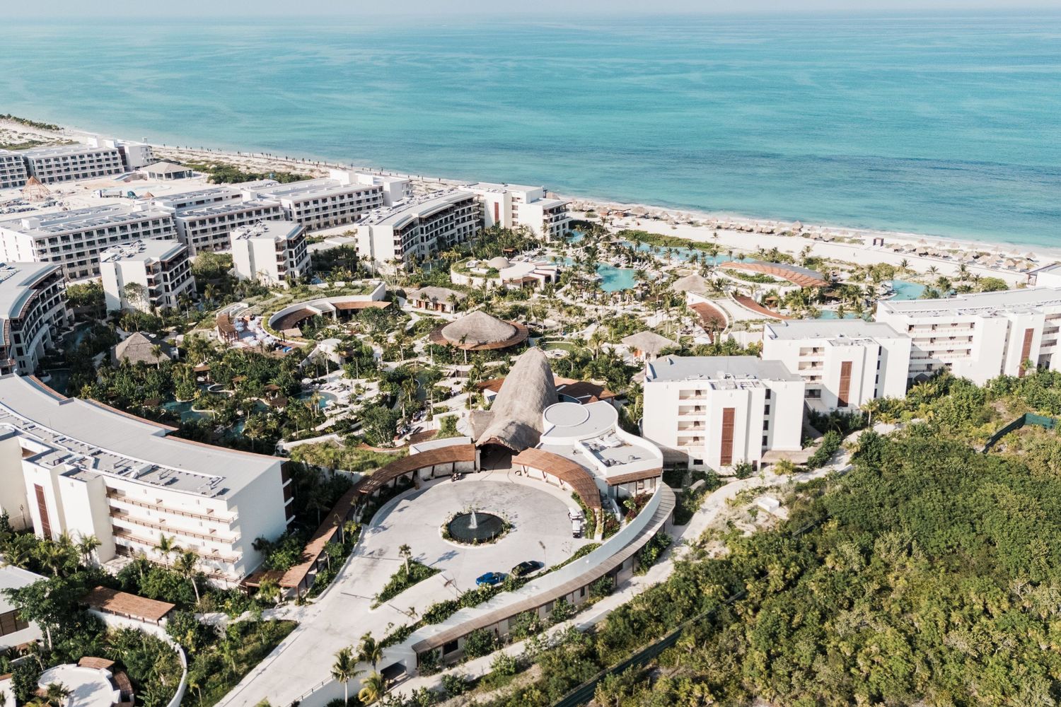 Aerial view of a luxury beachfront resort complex with pools, lush gardens, and ocean views.