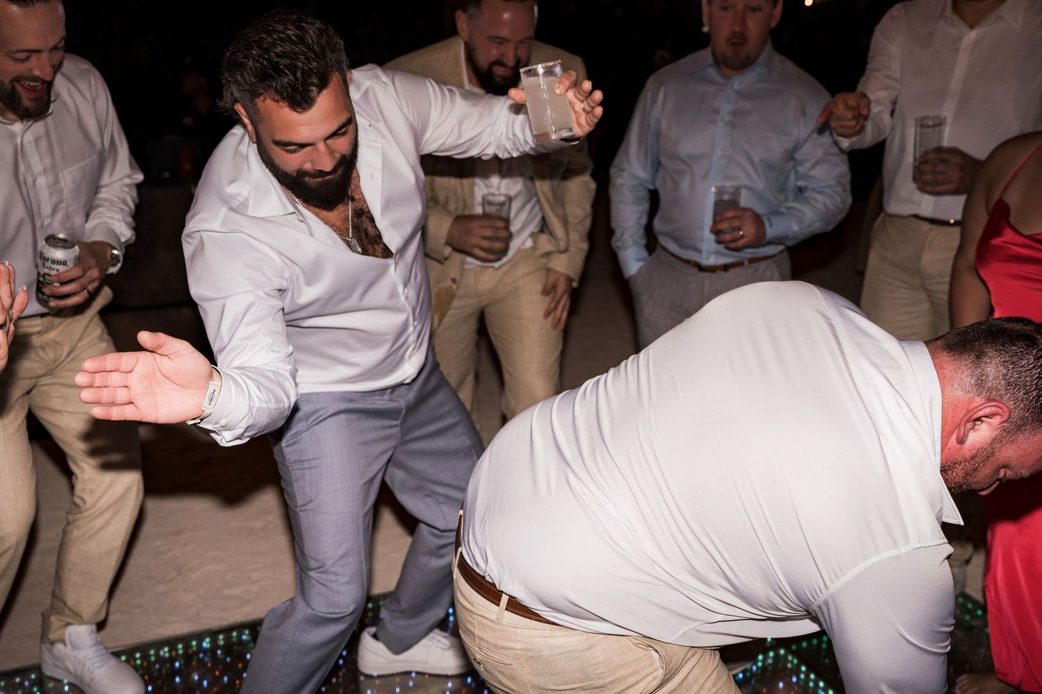 Men dancing energetically at a wedding reception party, wearing dress shirts and khakis under night sky.
