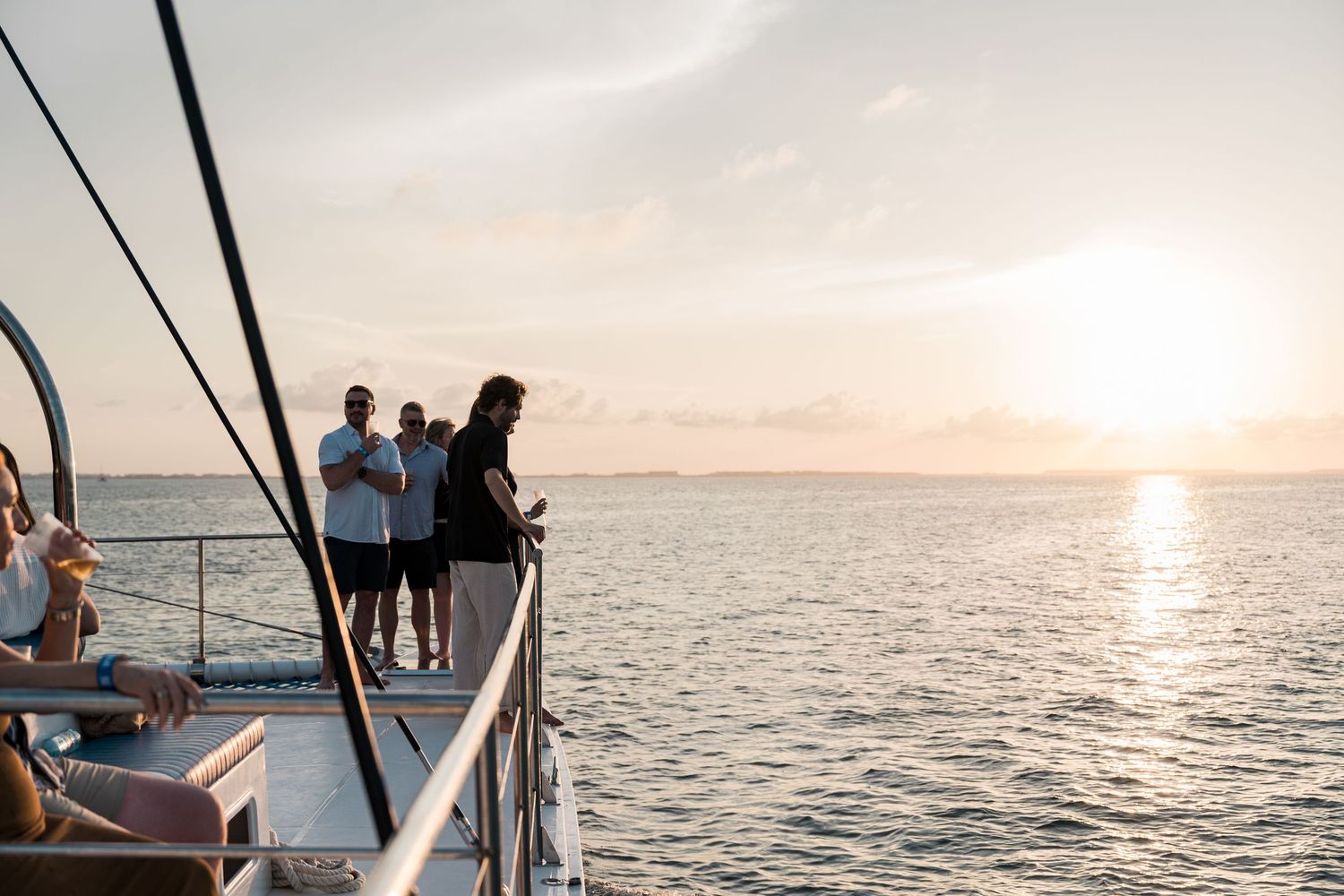 People enjoying a sunset cruise on a boat, standing on the deck watching the golden horizon over calm waters.