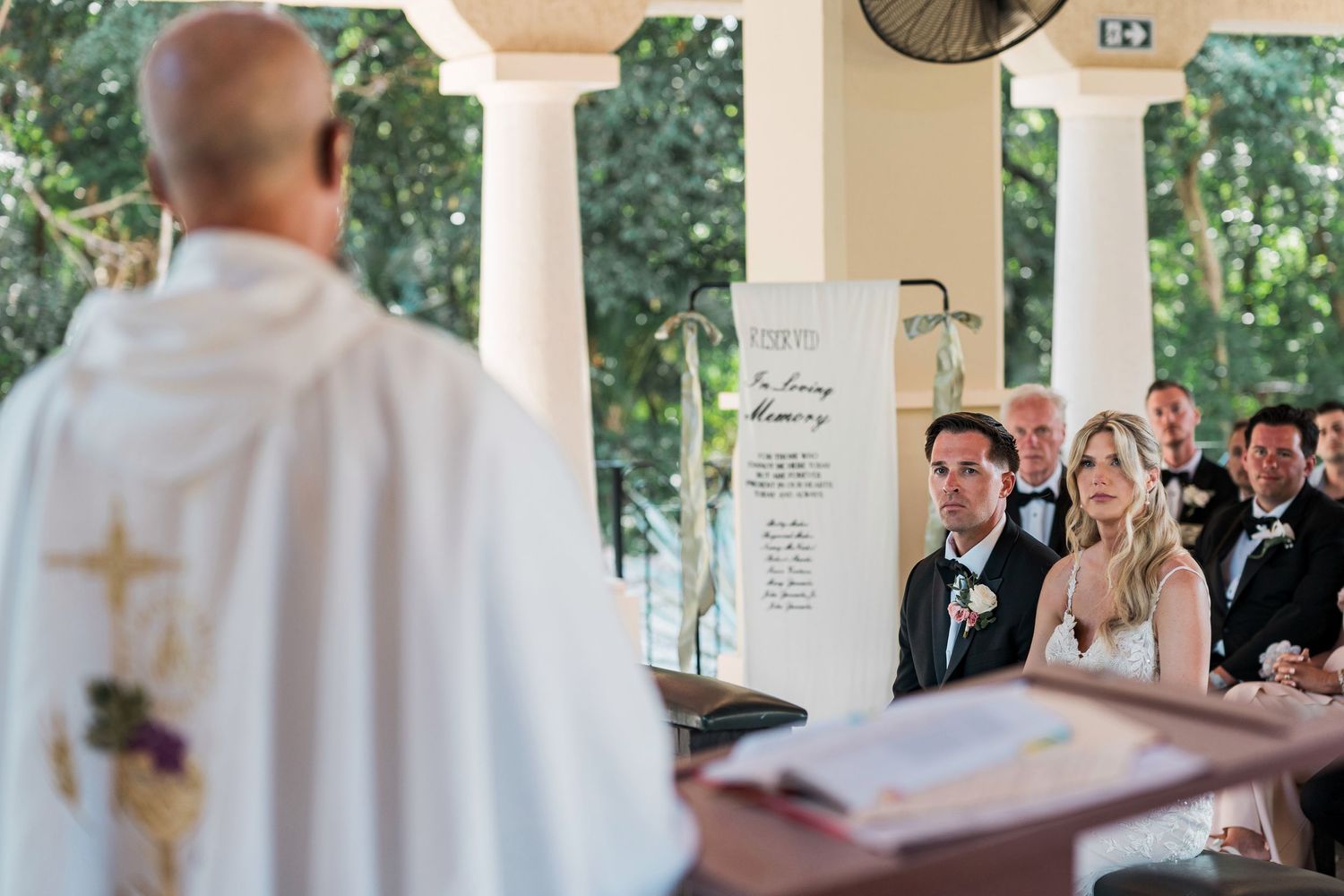 Priest officiating an outdoor wedding ceremony with bride and groom standing at the altar before guests.