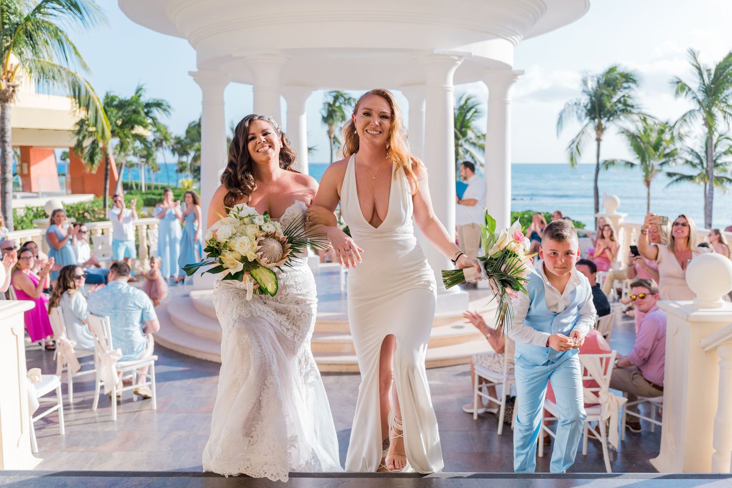 Two brides walking joyfully down the aisle after their beachside gazebo wedding ceremony.