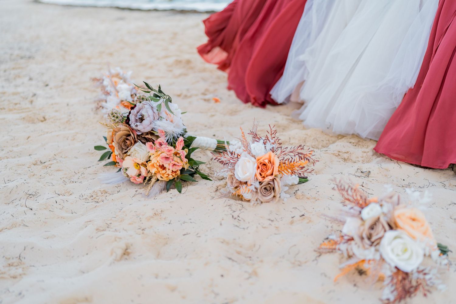 Colorful wedding bouquets with peach and coral roses resting on white sand beach.