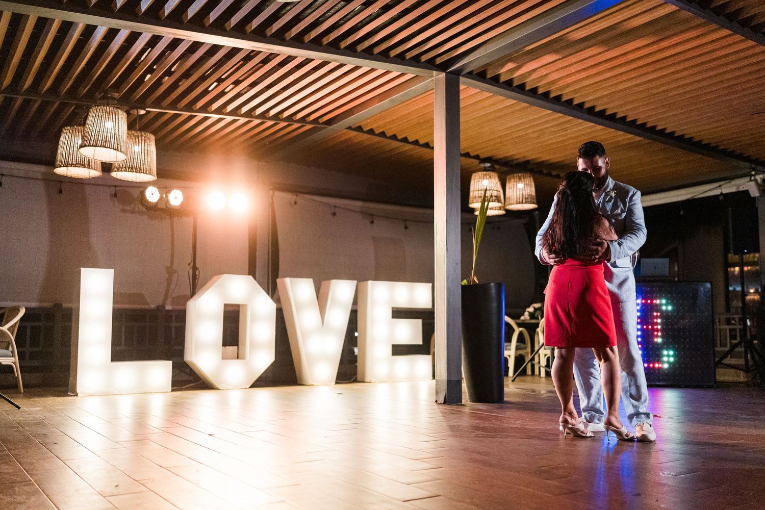 Couple shares romantic dance in front of large illuminated LOVE letters at wedding reception venue.