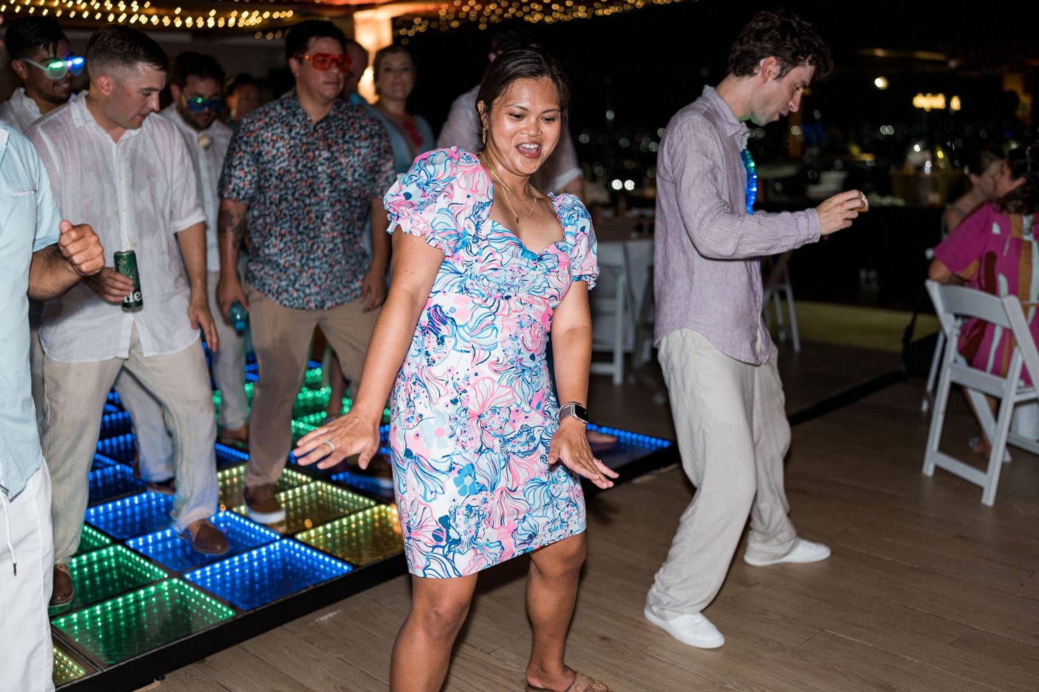 Woman in floral dress dancing joyfully on LED dance floor at outdoor wedding reception.