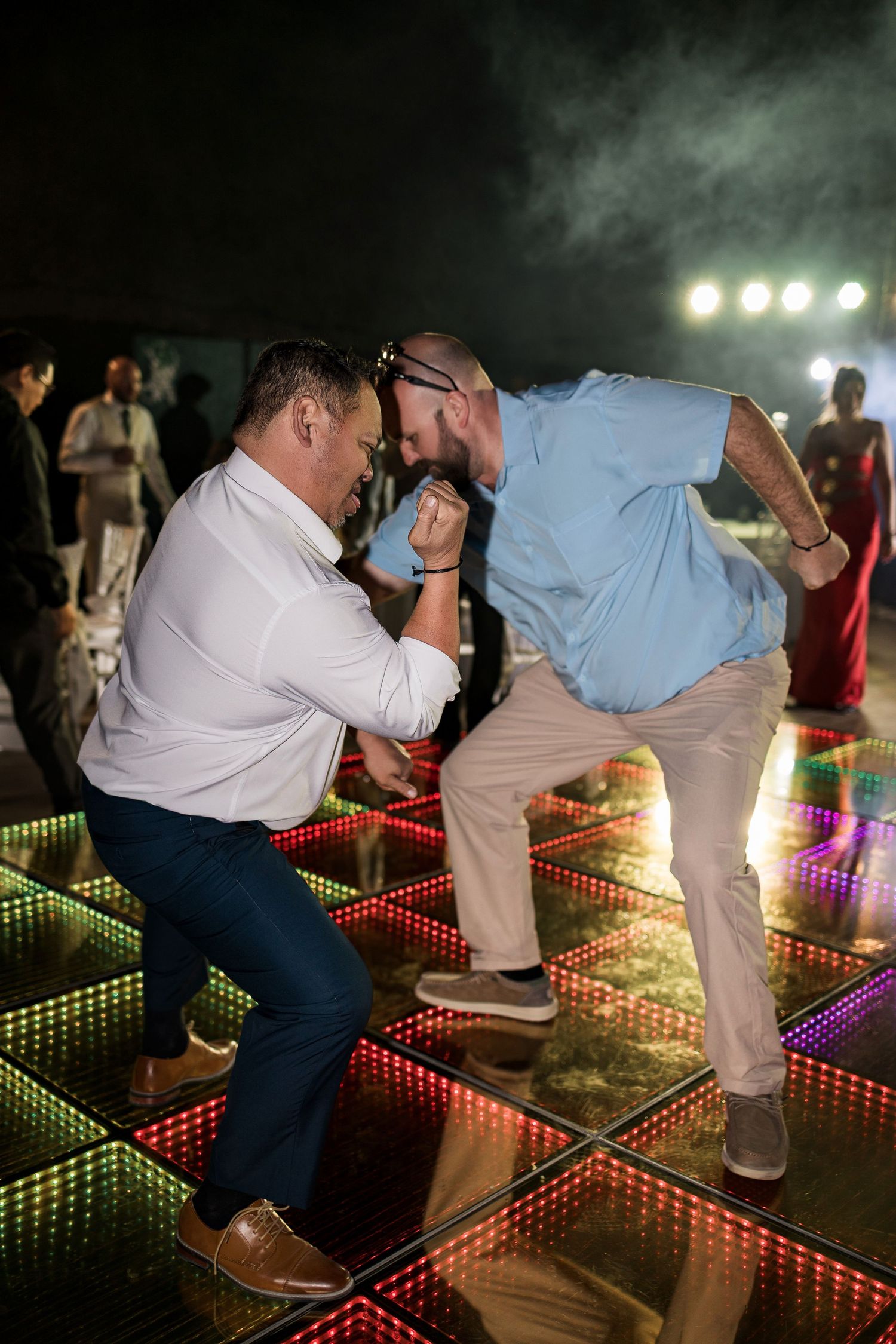 Two men dancing energetically on a colorful LED dance floor at a nighttime outdoor party event.