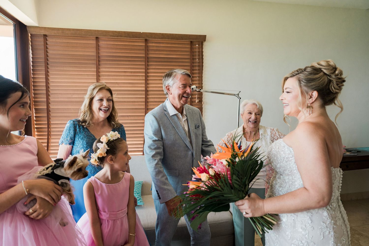 Bride in white gown holds colorful bouquet, smiling with family including flower girl and parents on wedding day.
