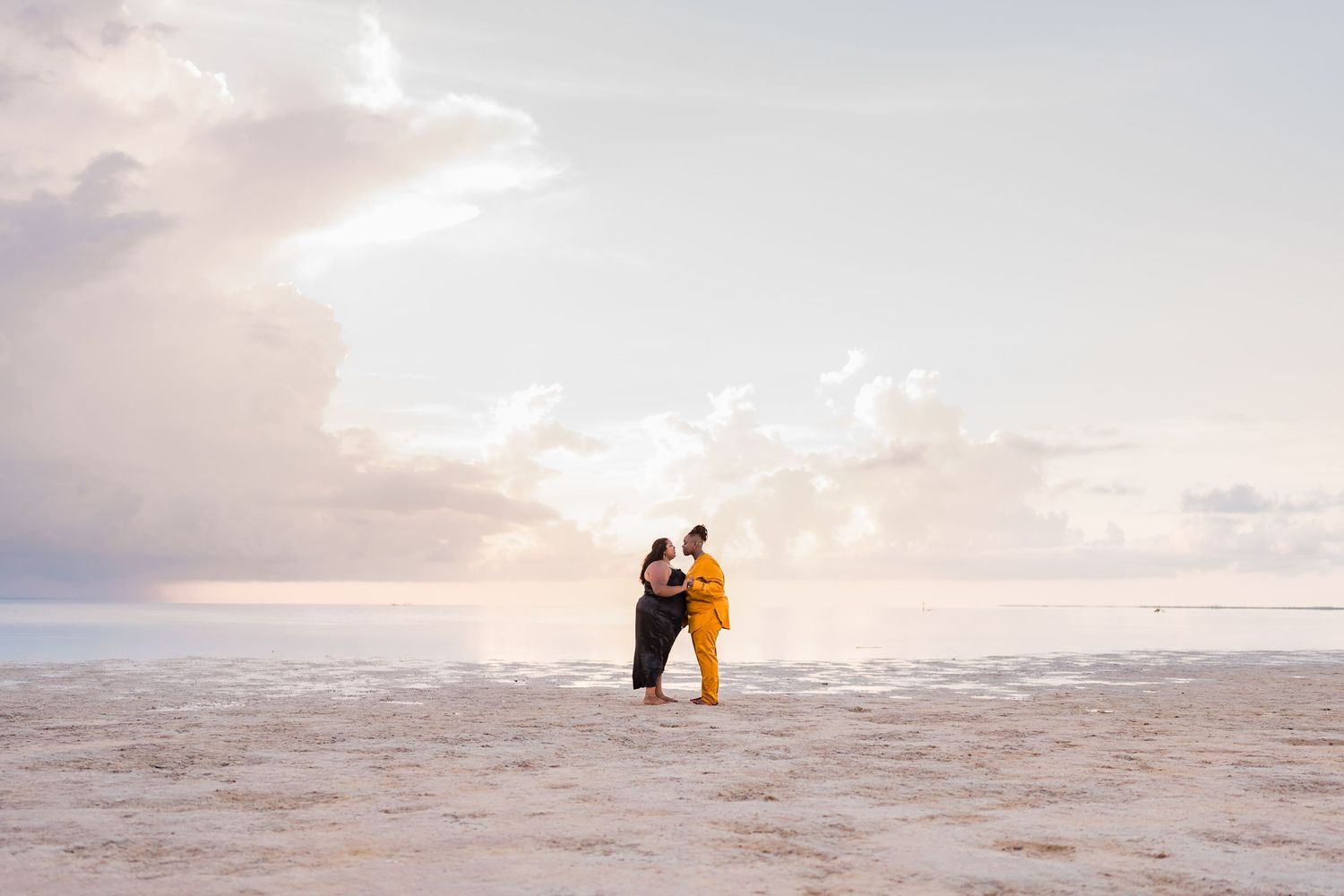 Two women holding each other on a serene beach at sunset.