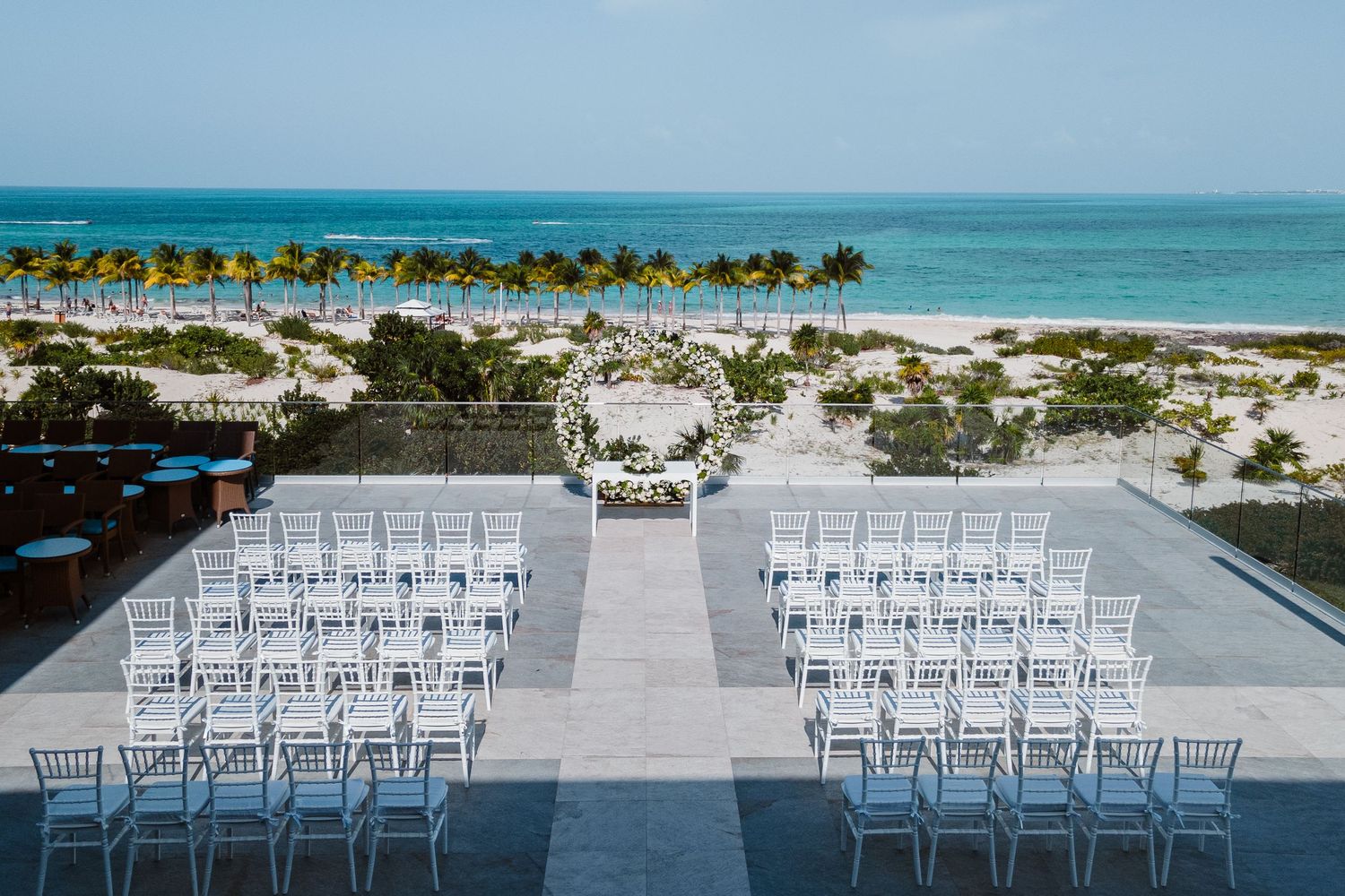 Elegant beachfront wedding ceremony setup with white chairs and floral arch overlooking ocean.