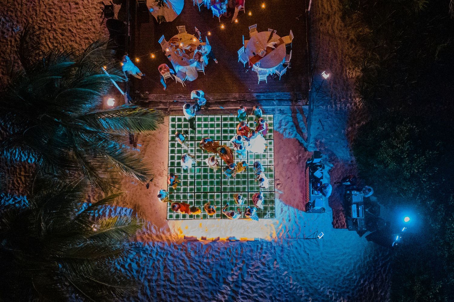 Aerial night view of outdoor wedding reception with string lights and palm trees.