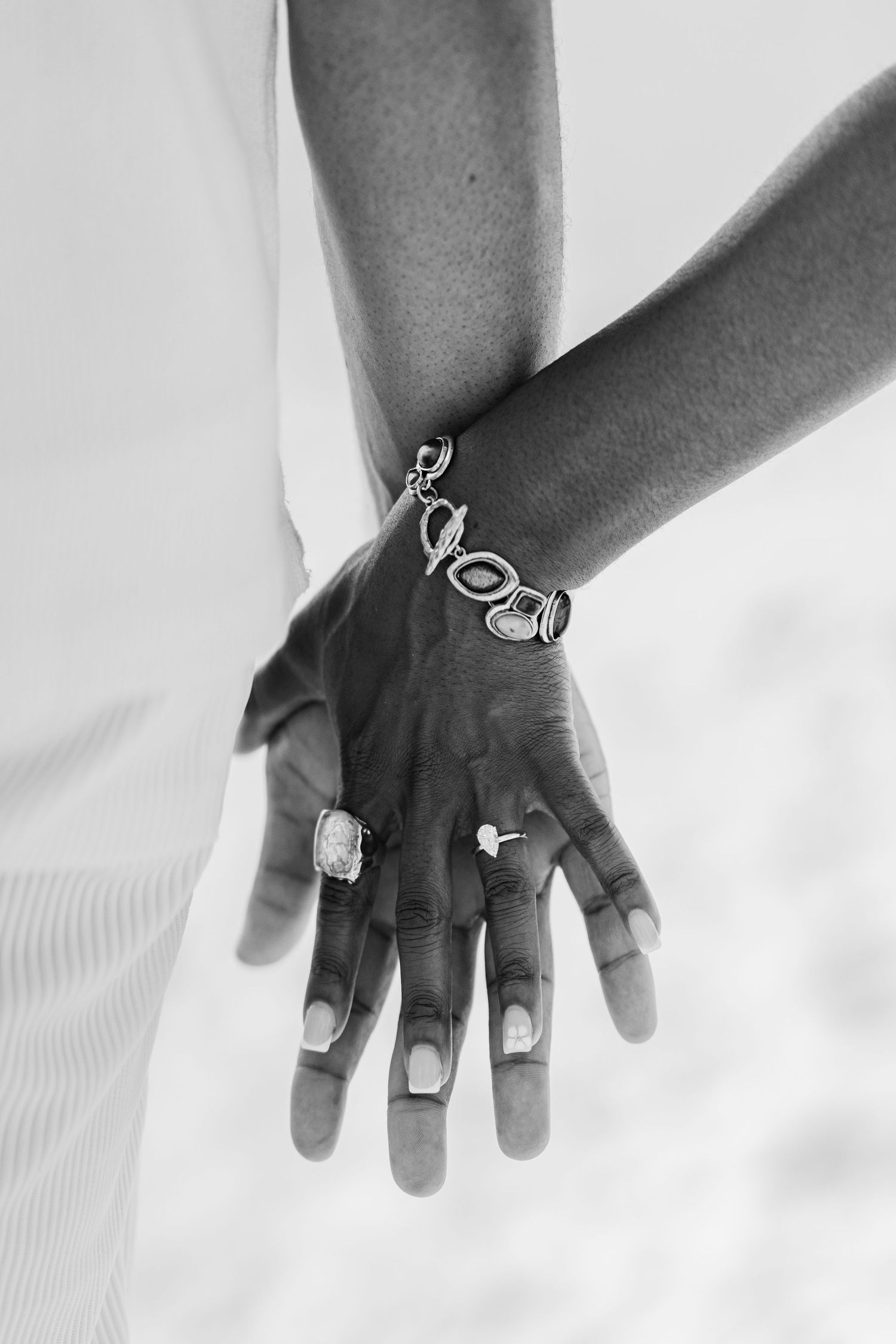 A black and white close-up of a couple holding hands, showing rings and a bracelet.