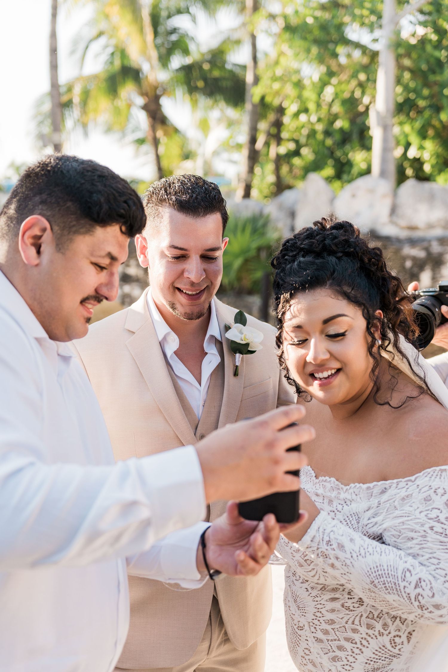 Xcaret Arte Wedding - Bride and groom smiling at phone with officiant at tropical beach wedding ceremony.
