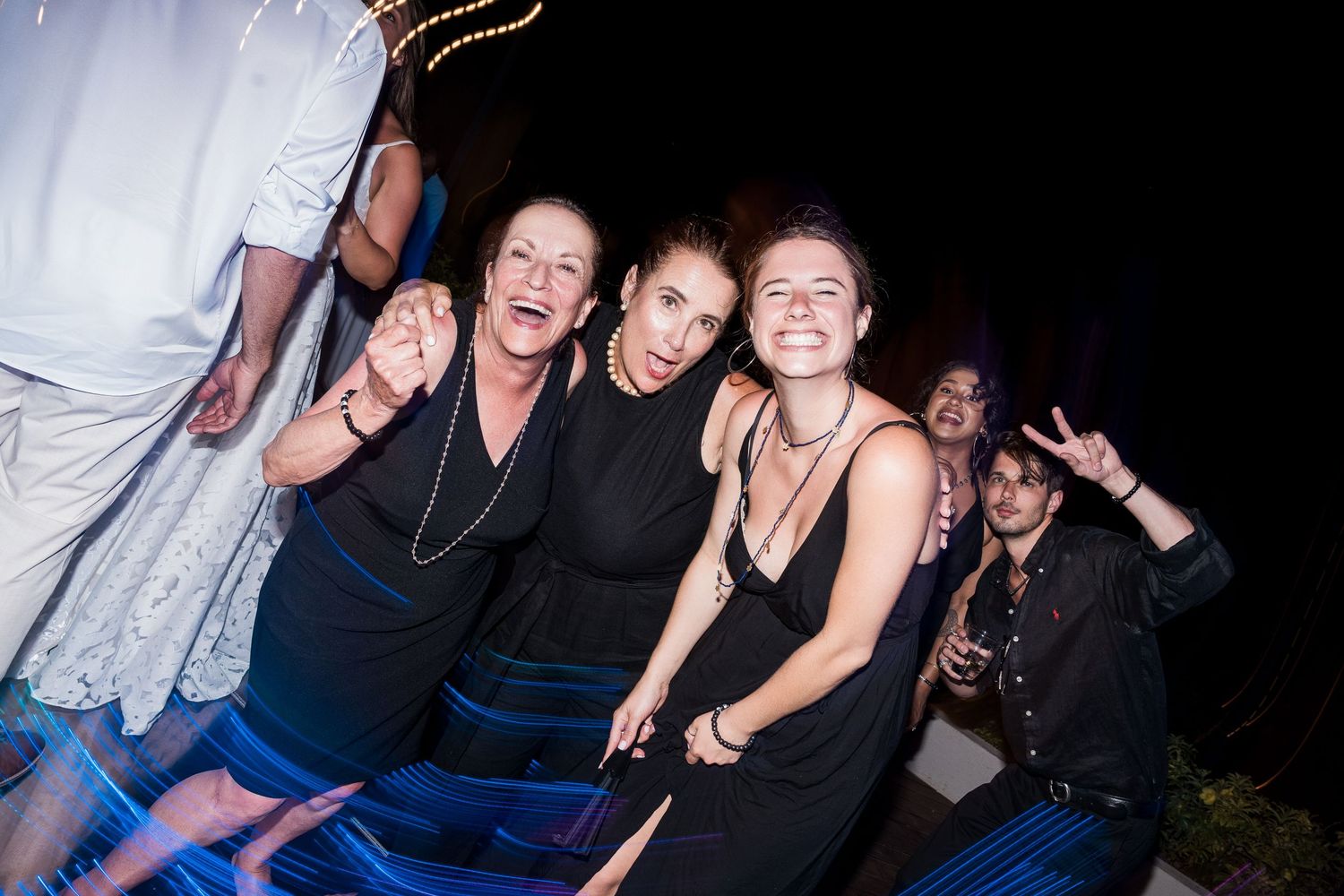 Three women in black outfits smile and pose together at an outdoor nighttime party event.