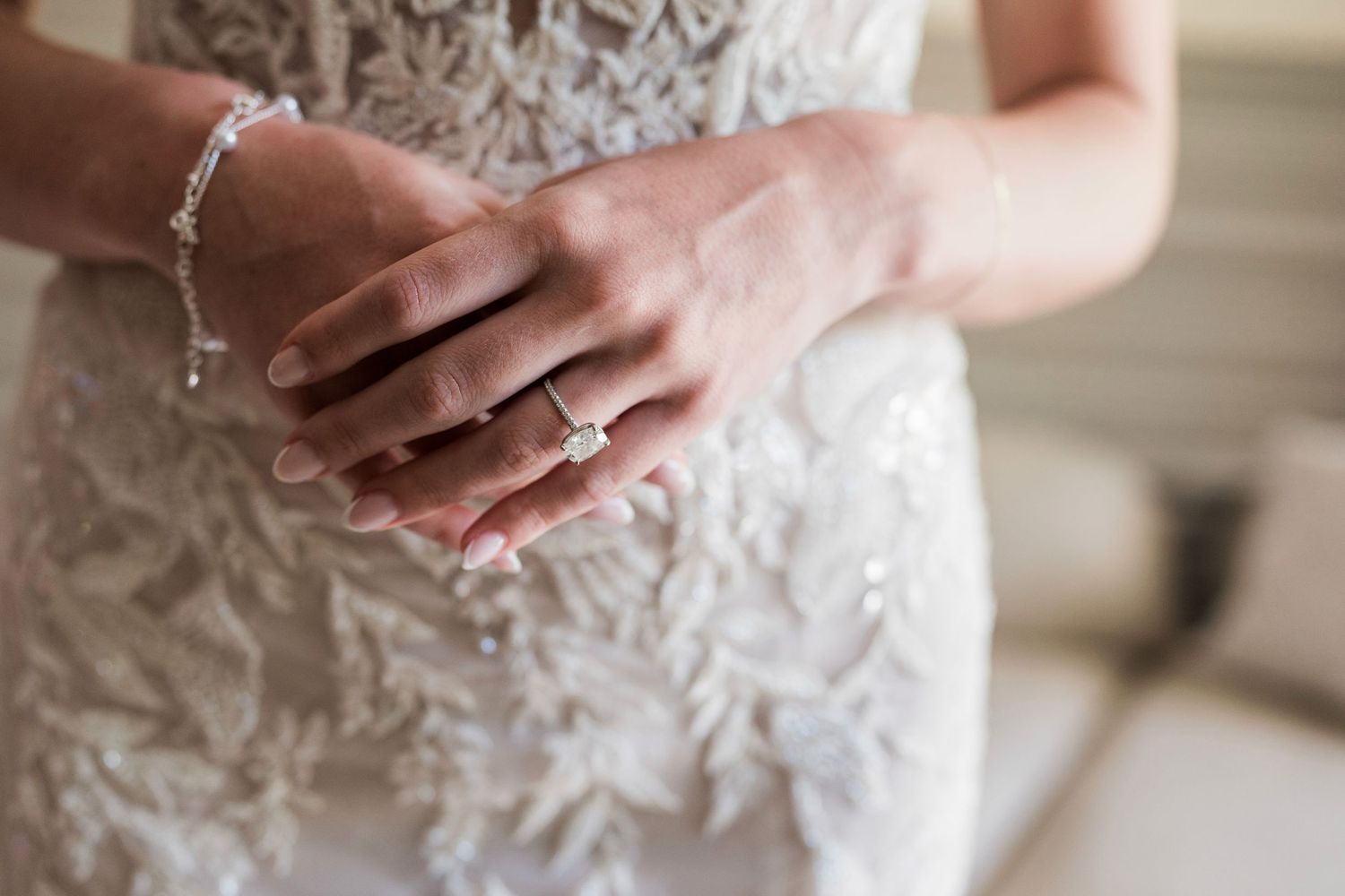 Bride in lace wedding dress showcasing diamond engagement ring and delicate bracelet on her hands.