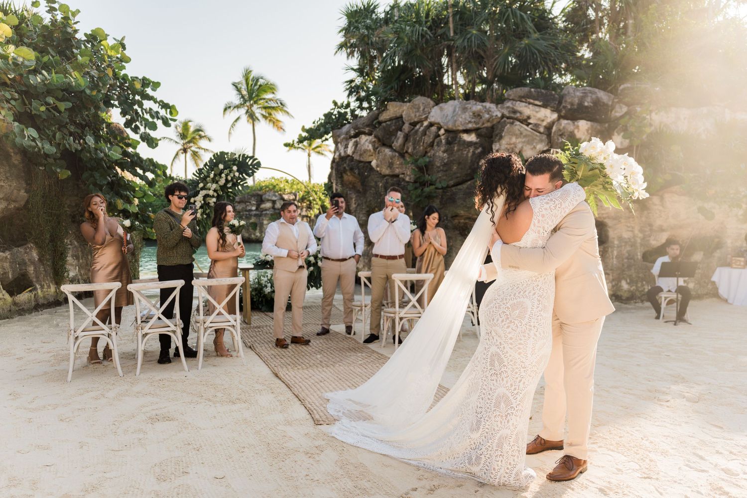 Xcaret Arte Wedding - Bride and groom share first dance on sandy beach wedding venue with guests and tropical rock backdrop.