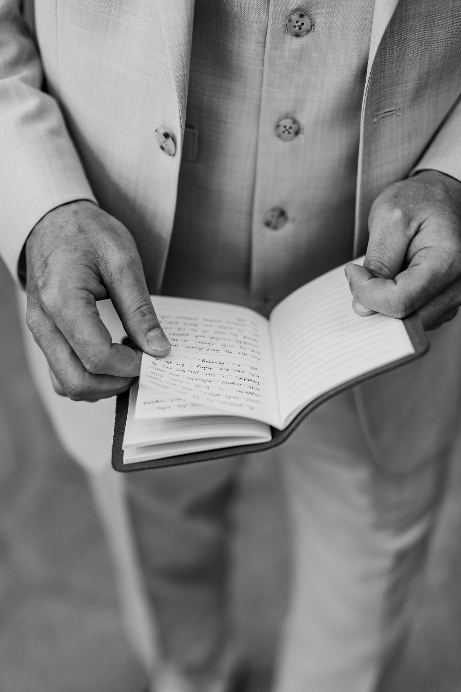 Black and white photo of a man in a suit holding an open small notebook with handwritten notes.