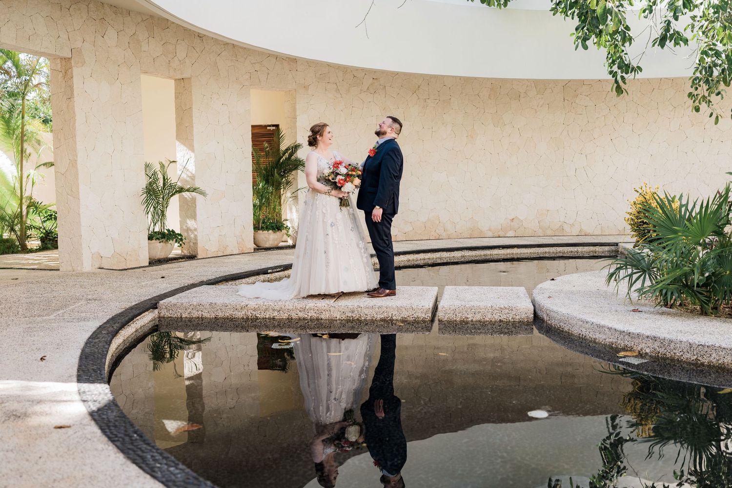 Secrets Akumal Wedding - Bride and groom stand facing each other by a reflective pool in an elegant outdoor venue