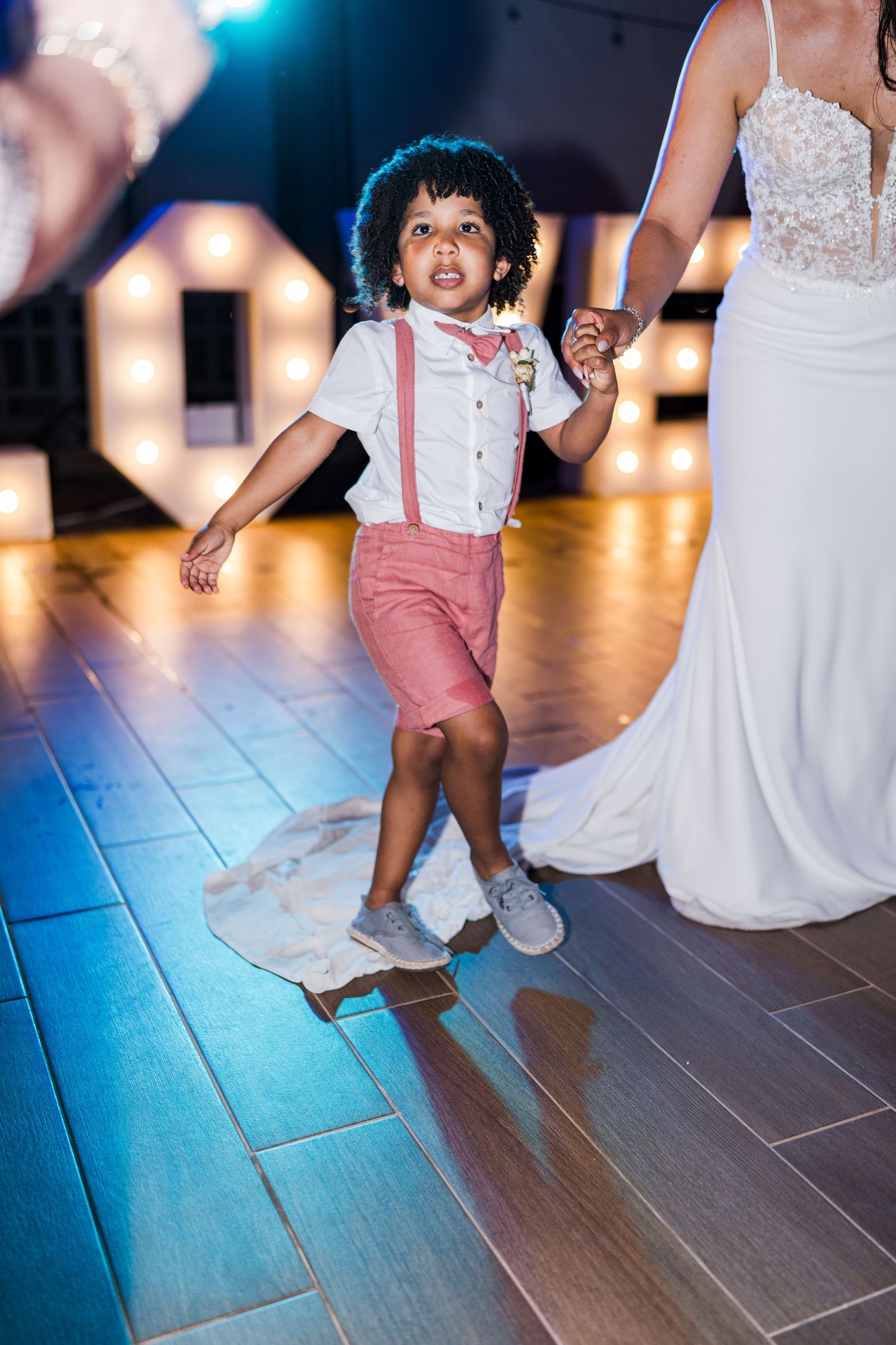 Adorable young ring bearer in suspenders and bow tie dancing at a wedding reception.
