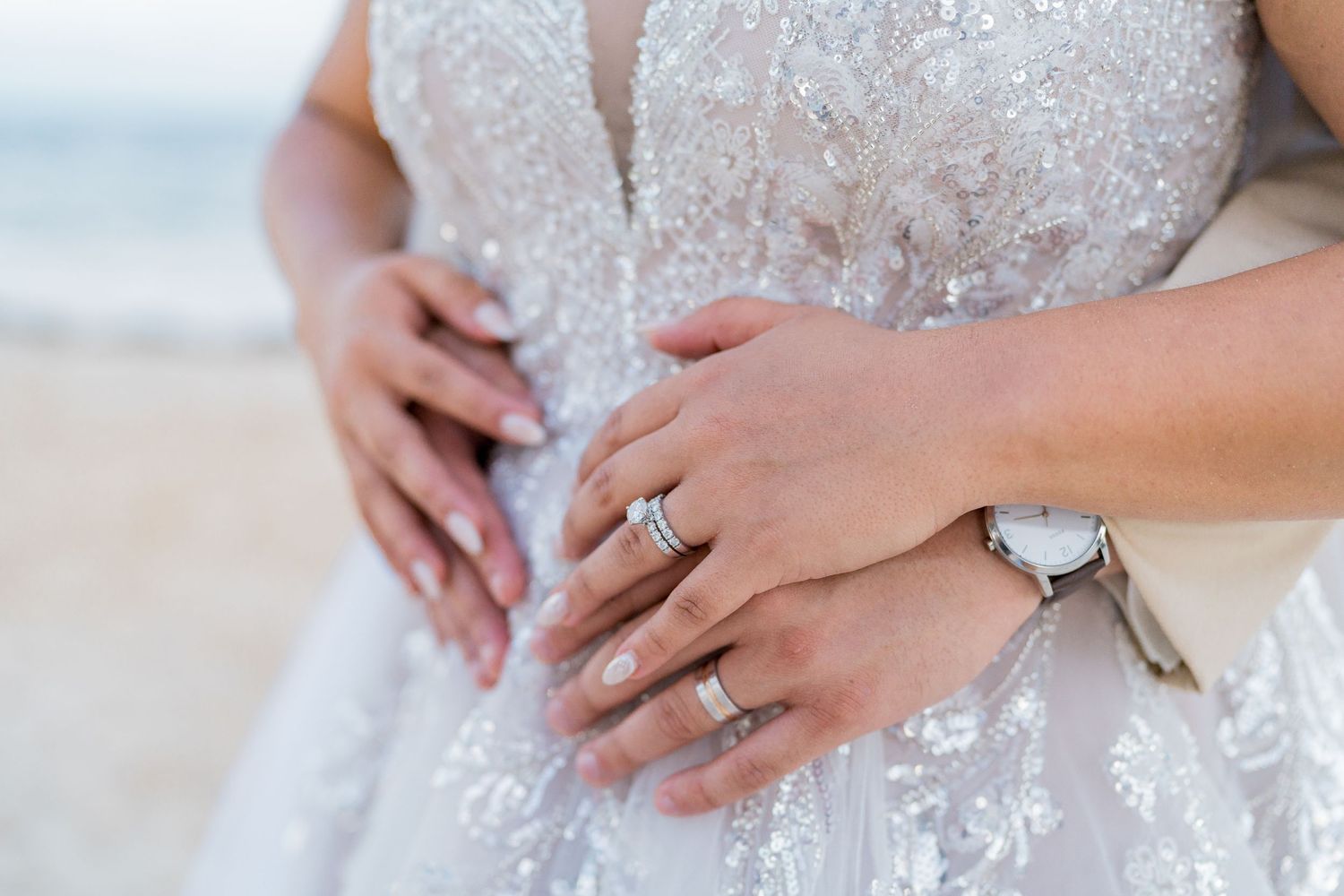 Close-up of bride and grooms hands showing wedding rings on lace bridal gown.