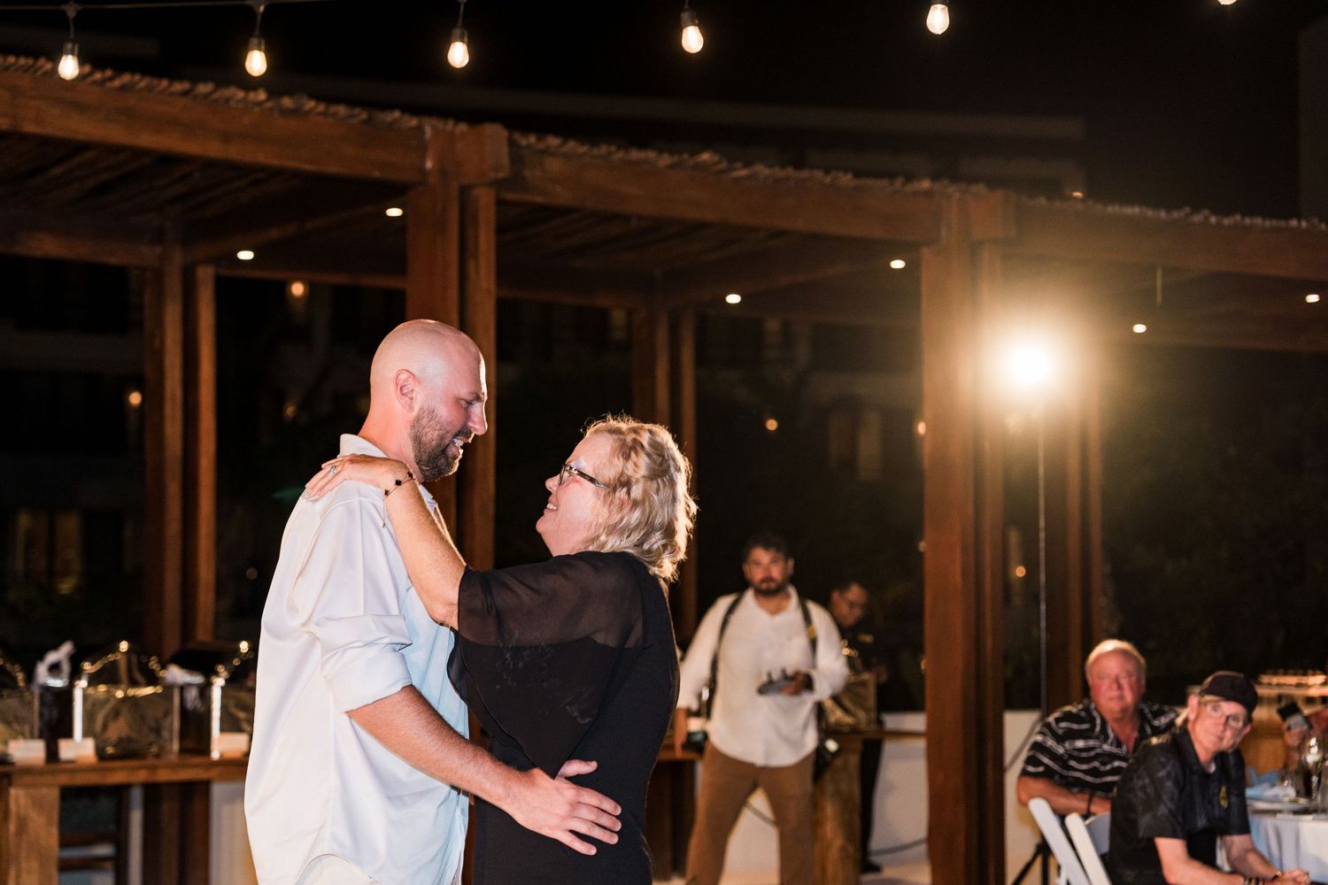 Couple shares a romantic first dance at an outdoor evening wedding reception with string lights.