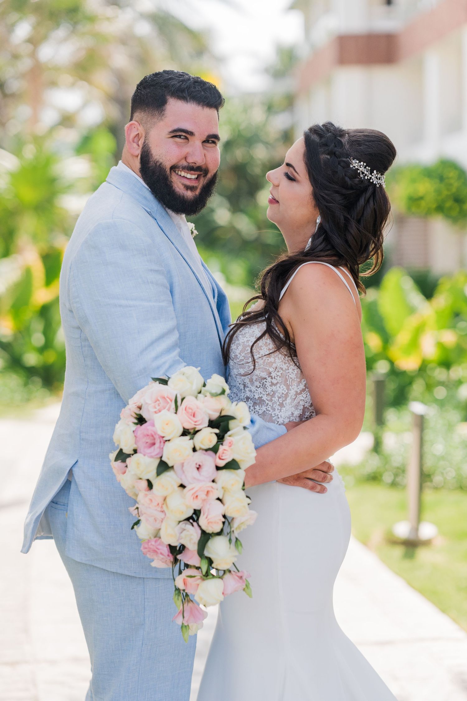 Joyful groom in light blue suit laughing with bride holding cascading pink and white rose bouquet.