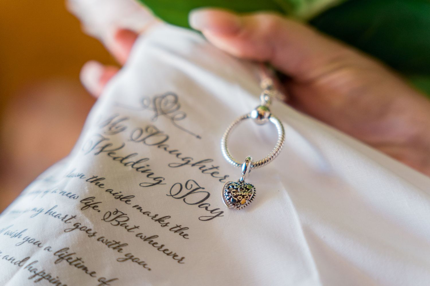 Close-up of a silver heart charm keychain on a white handkerchief with a heartfelt daughter wedding day message.