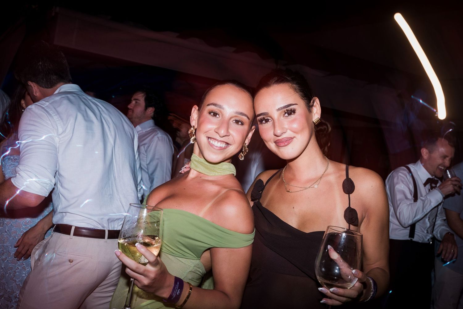 Two smiling women holding wine glasses pose together at an indoor party event. TRS Yucatán Hotel Wedding
