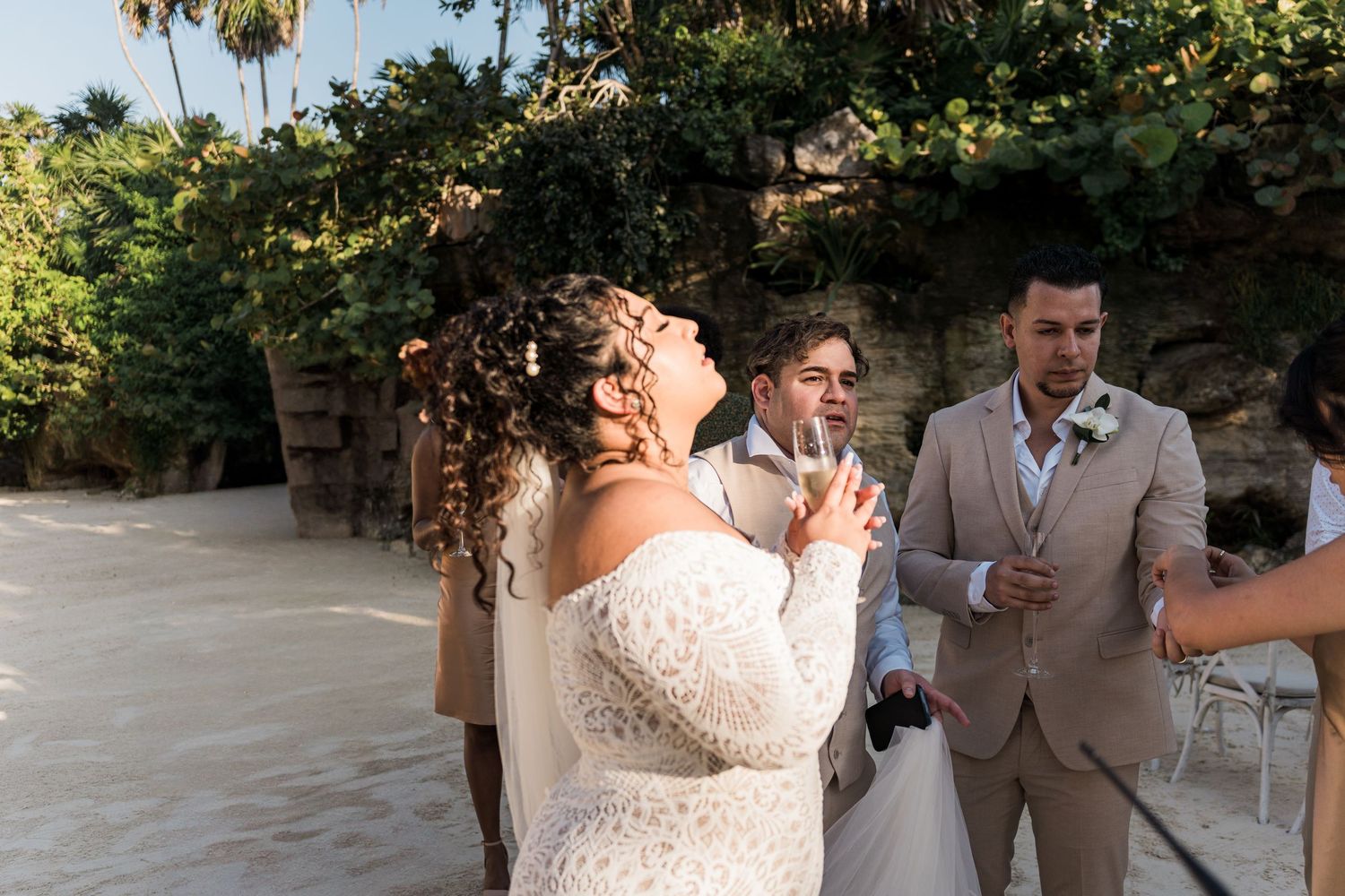 Xcaret Arte Wedding - Bride in white off-shoulder gown laughs joyfully during outdoor beach wedding ceremony with groom in tan suit.