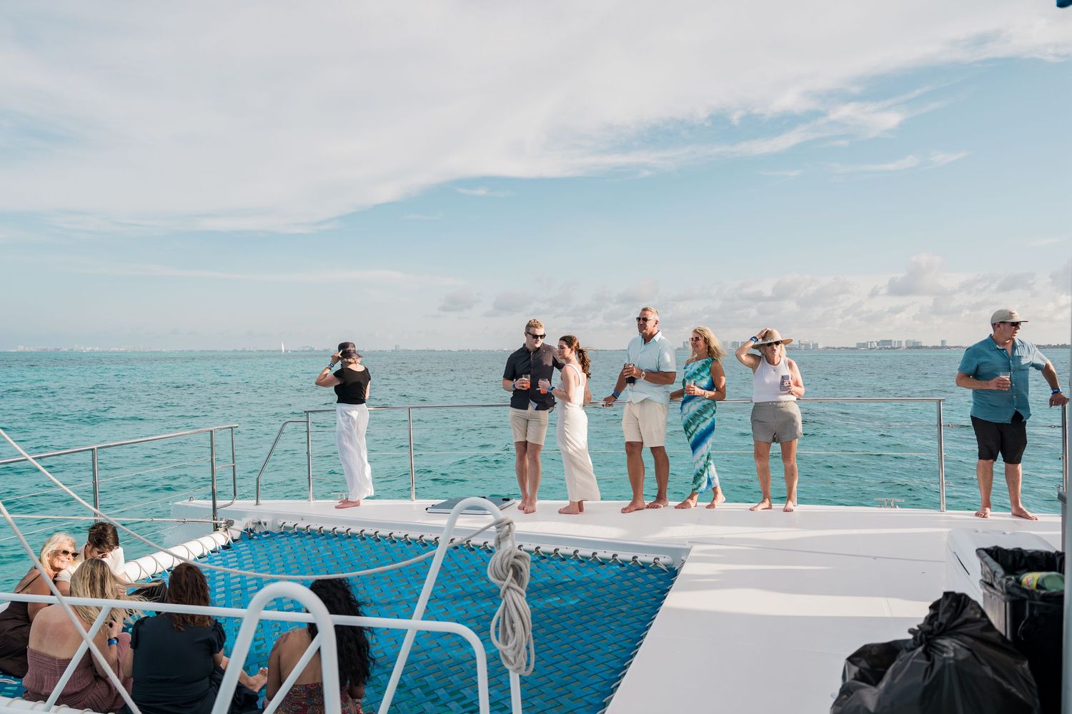 Group of people standing on a catamaran deck overlooking turquoise ocean waters on a sunny day.