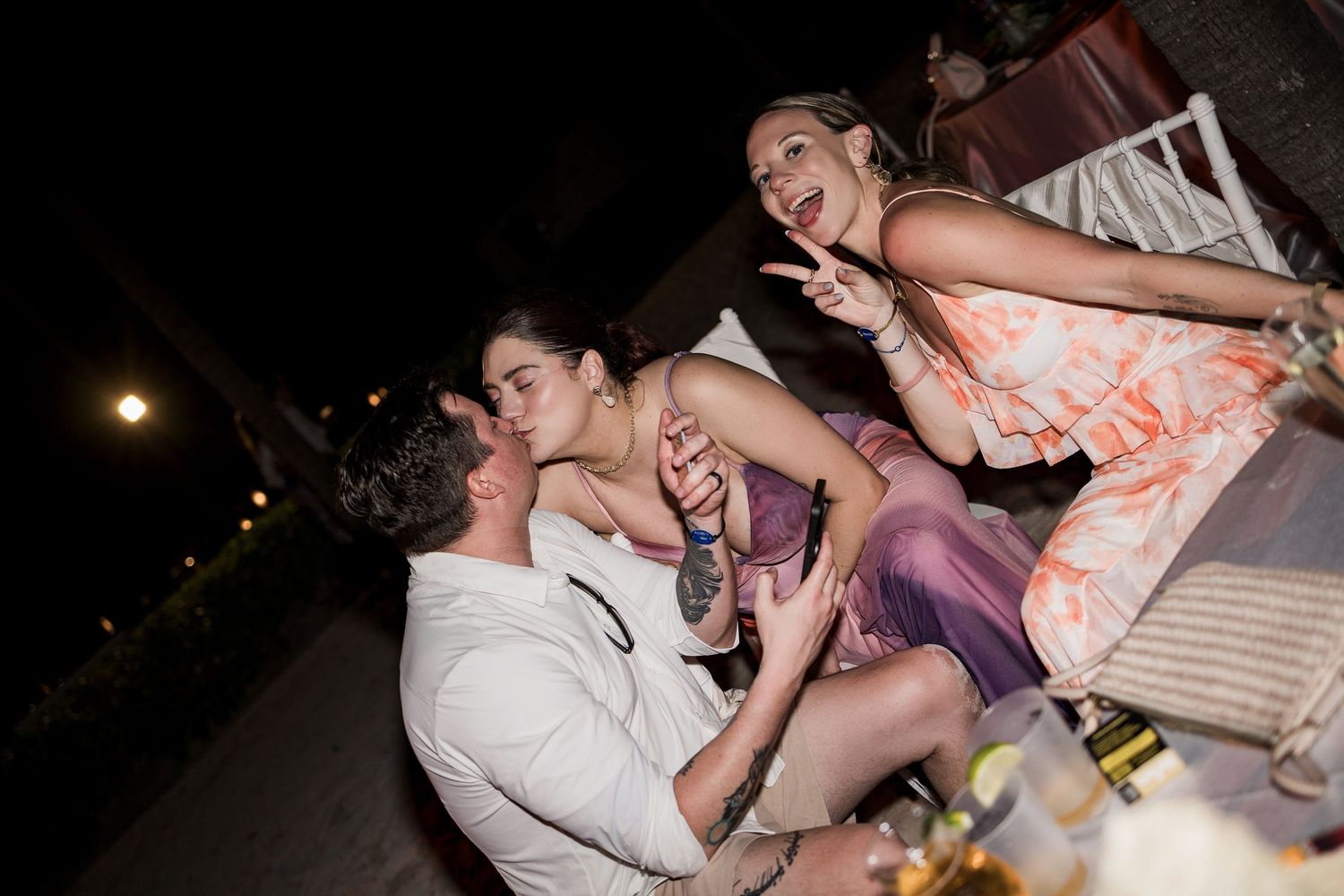 Three friends laughing and celebrating together at an outdoor evening party event.