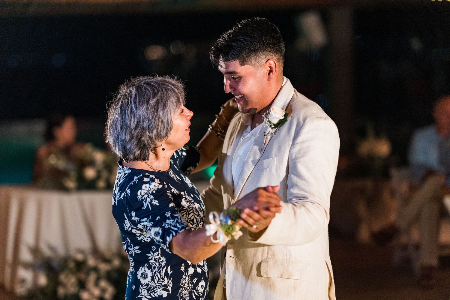Groom shares a tender mother-son dance at wedding reception under evening lights.
