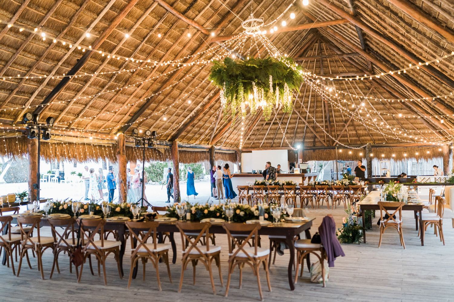 Rustic tropical wedding reception venue with thatched roof, string lights, and wooden tables.