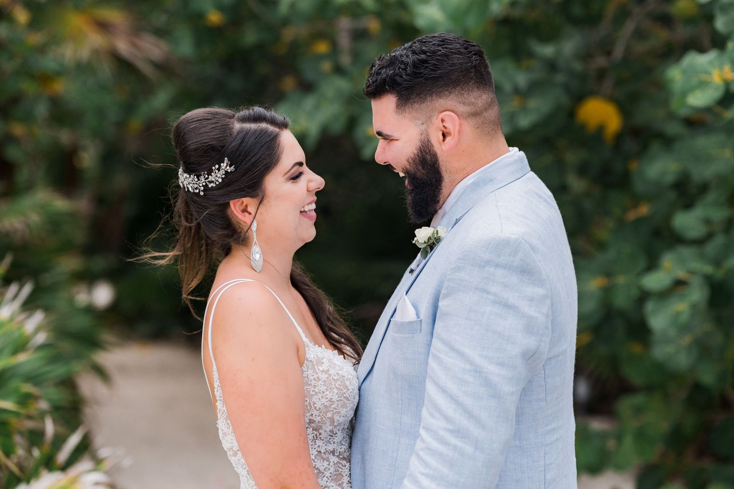 Bride and groom gazing at each other and smiling in front of tropical green foliage.