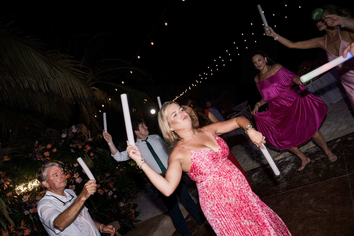 Guests dancing with glow sticks at an outdoor evening wedding reception party.