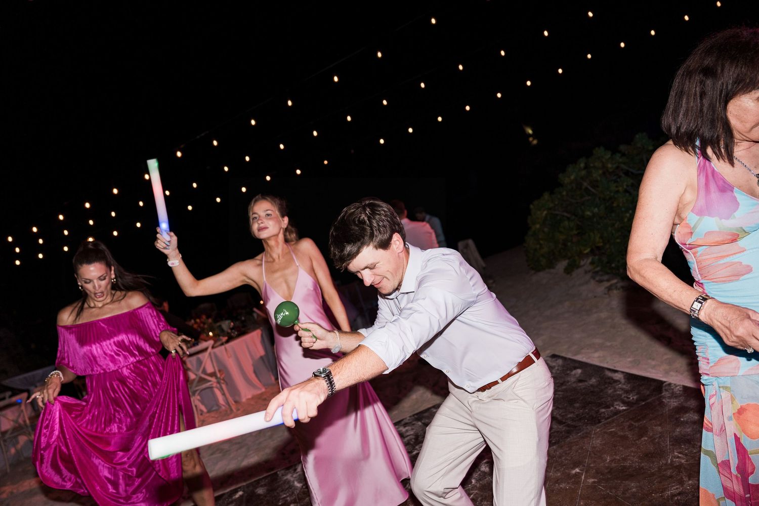 Guests dancing and playing with glow sticks at an outdoor evening wedding reception party.