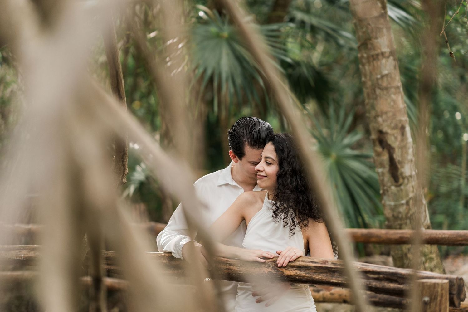 Couple embracing tenderly in a lush tropical garden, framed by bamboo and palm trees in a romantic outdoor setting.