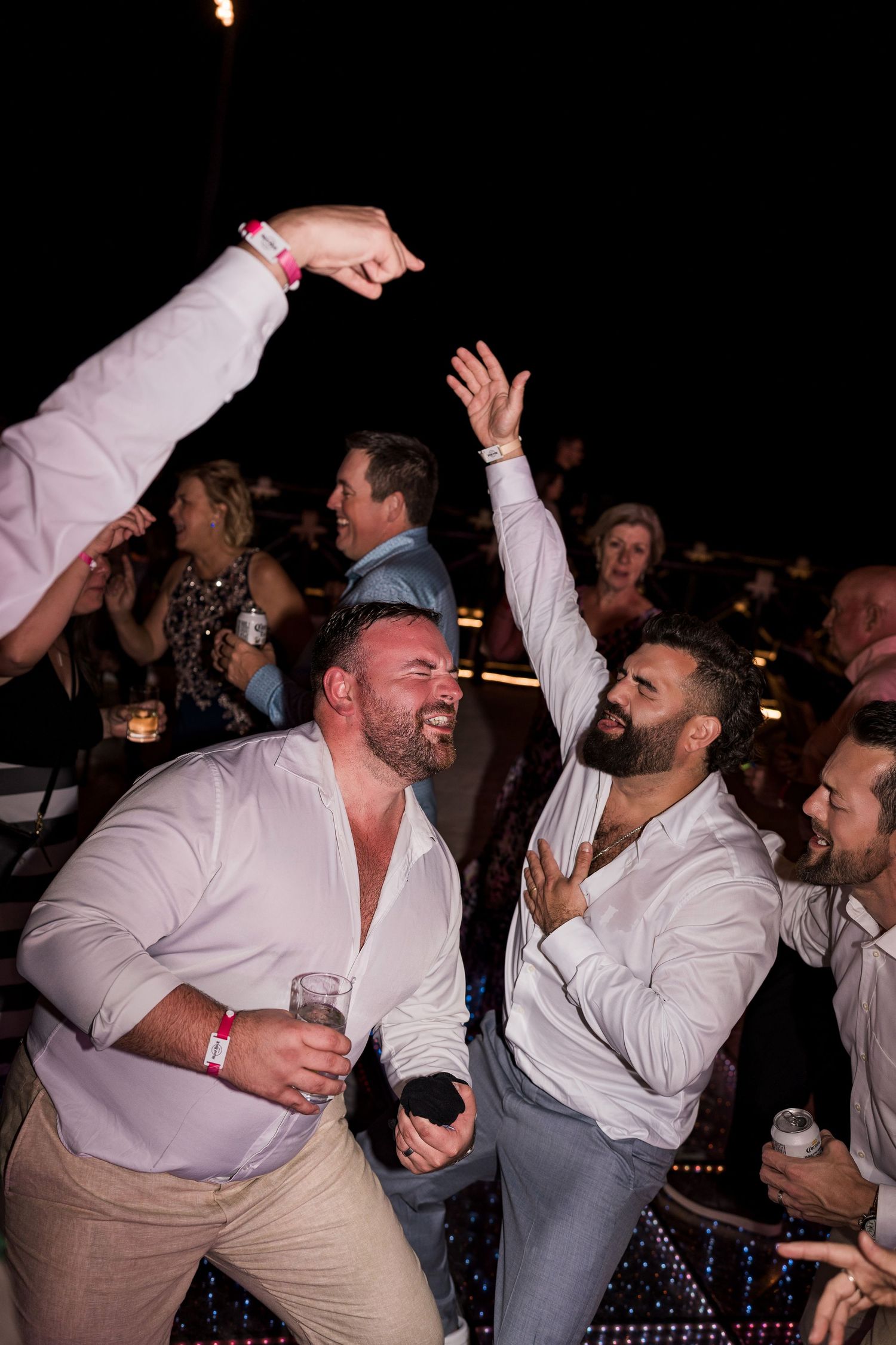 Two men in white shirts dancing and celebrating at an outdoor evening party event.