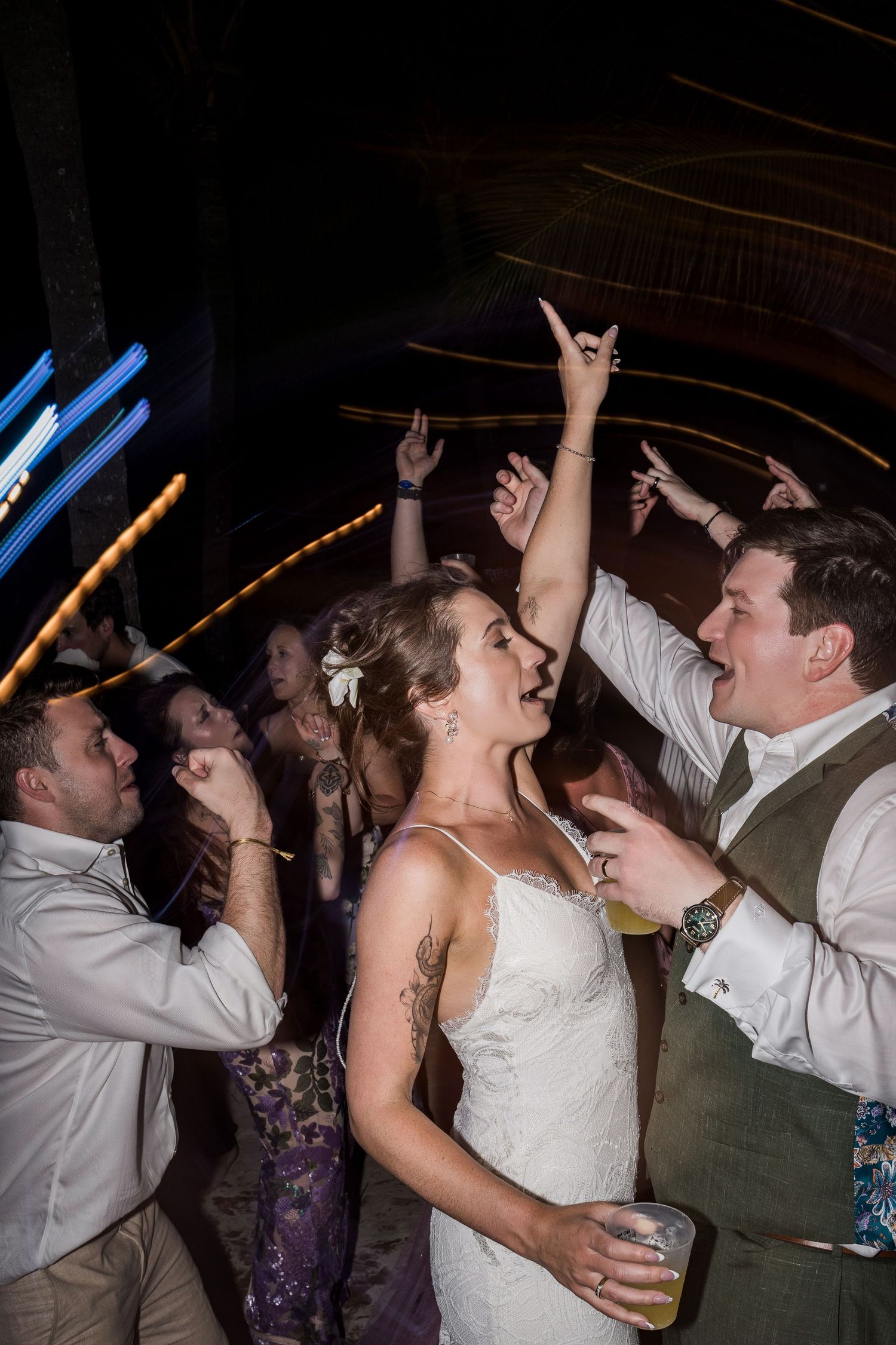 Bride and groom dancing joyfully with guests at a lively wedding reception party under dim lights.