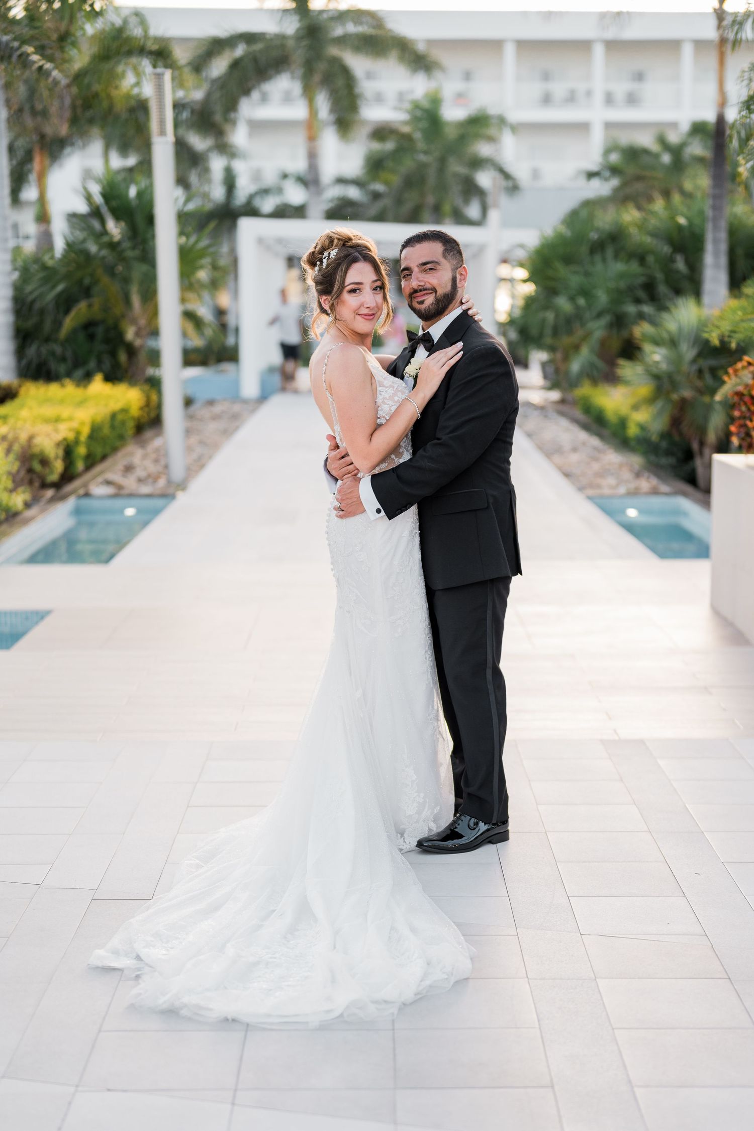 Bride and groom pose elegantly together at a tropical resort with palm trees.
