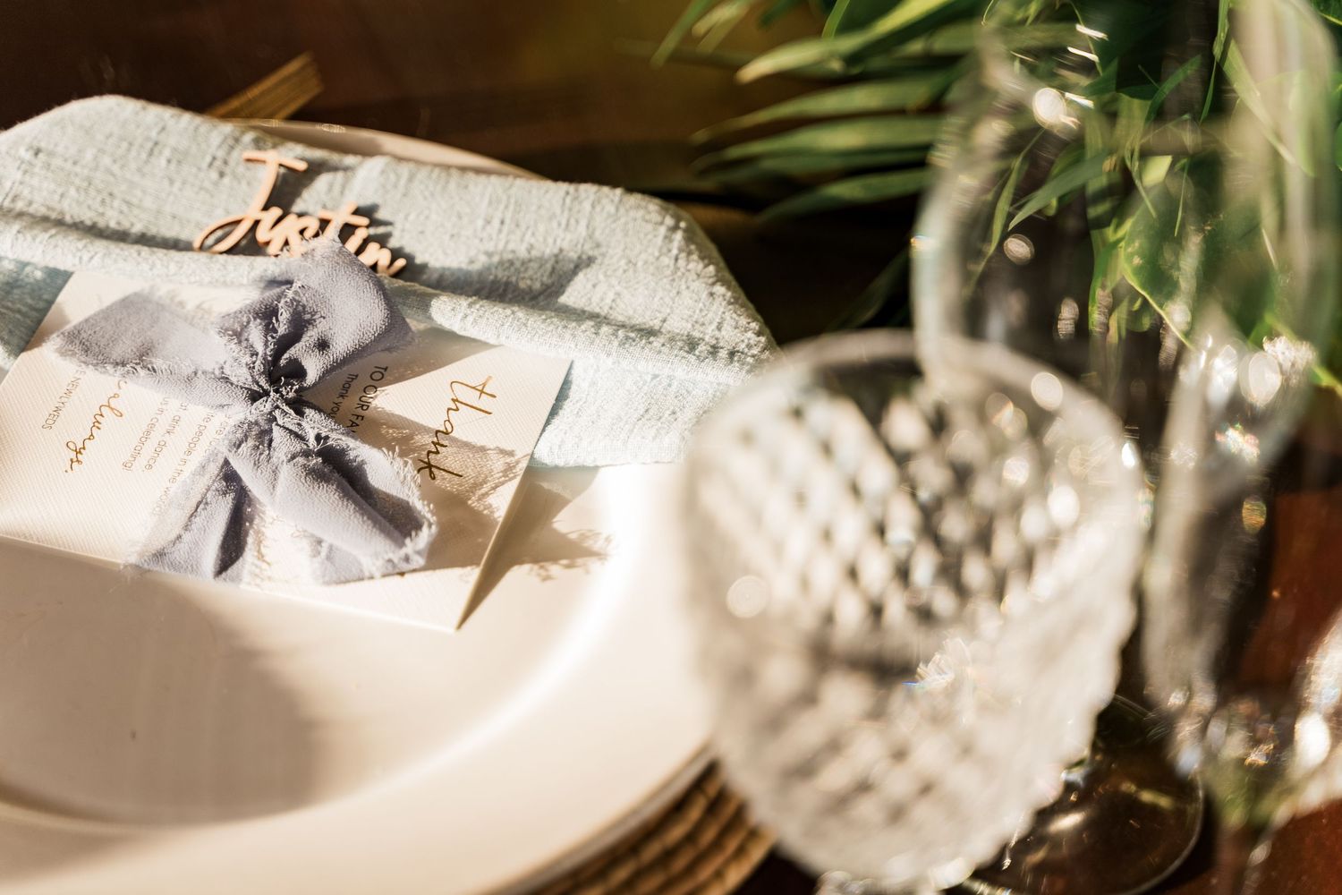 Elegant wedding place setting with calligraphy name card, floral menu, and crystal glassware on a rustic table.