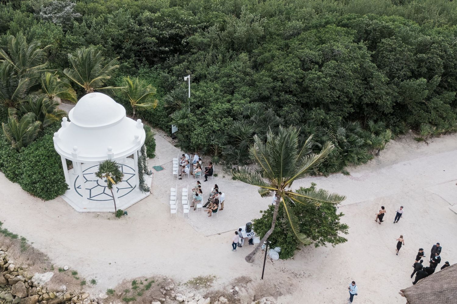 Aerial view of a white gazebo wedding ceremony venue surrounded by lush tropical palm trees.