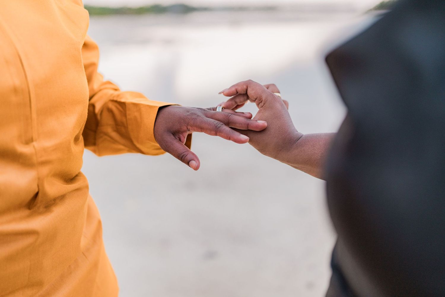 Close-up of hands exchanging a ring during a beach proposal or wedding ceremony.