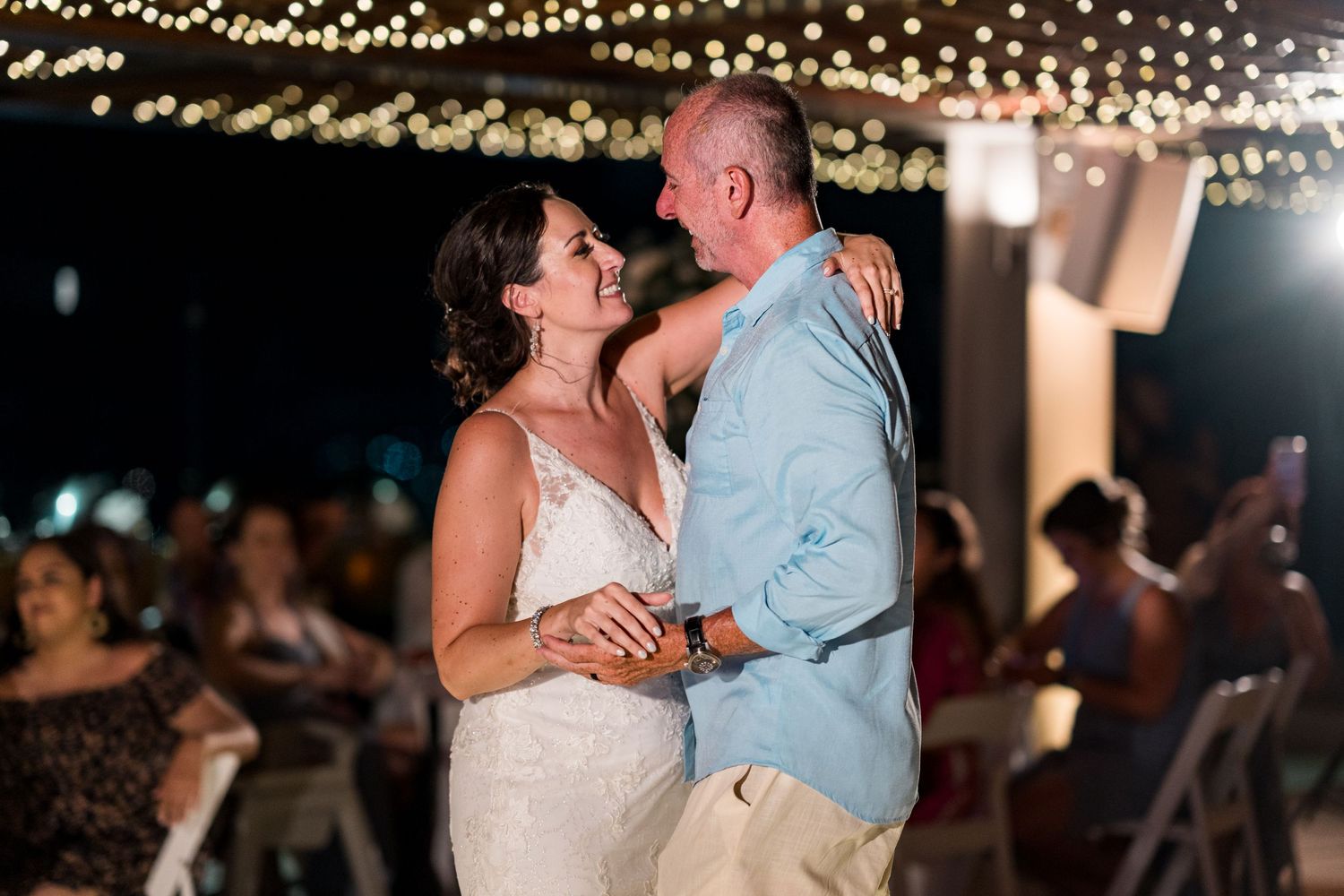 Bride and groom share a romantic first dance under twinkling fairy lights at an outdoor wedding reception.