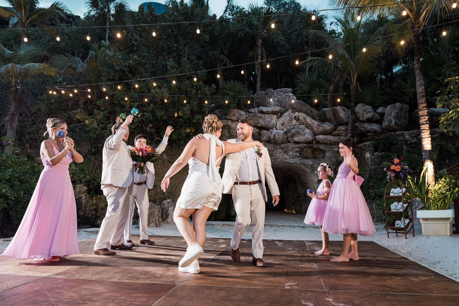 Hotel Xcaret México Bride and groom dance with guests at outdoor wedding reception with string lights and tropical backdrop.