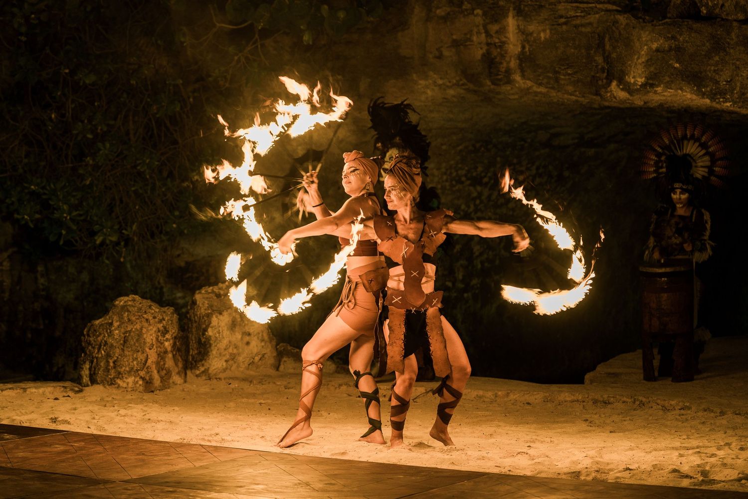 Hotel Xcaret Mexico - Two fire dancers in traditional Mayan costumes perform a mesmerizing fire dance in a dimly lit cave setting.