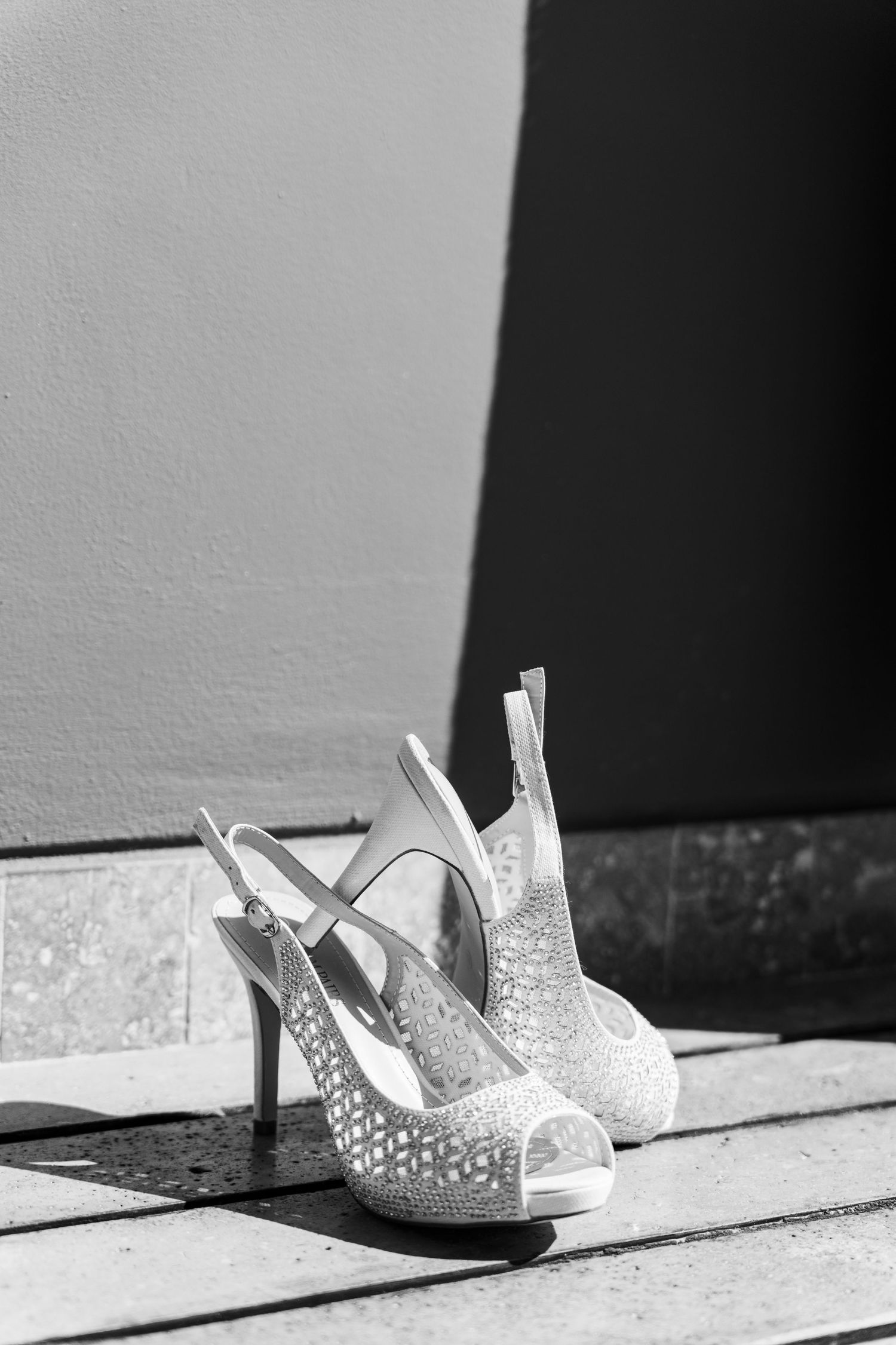 Xcaret Arte Wedding - Elegant white glitter peep-toe slingback heels placed on wooden surface in black and white photography.