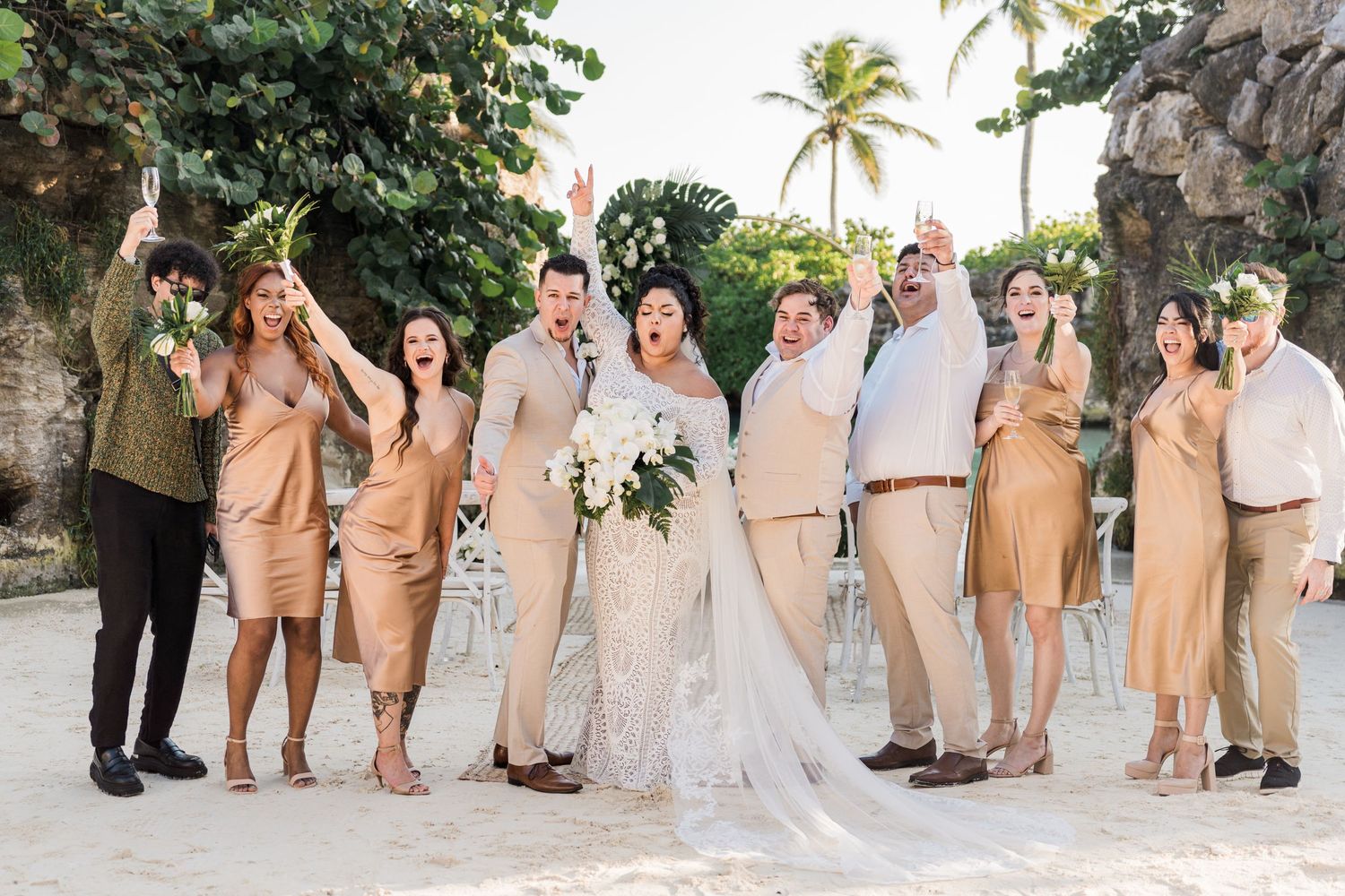 Xcaret Arte Wedding - Wedding party celebrating on a tropical beach in neutral tones, bride in white gown with bouquet.