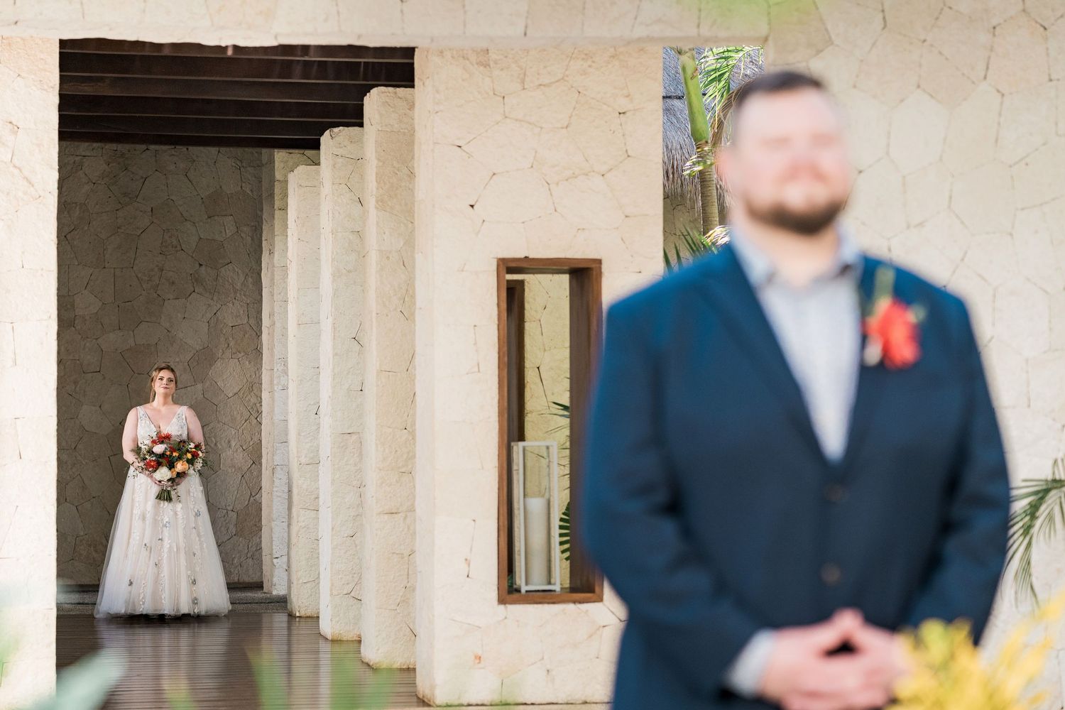 Secrets Akumal Wedding - Bride in white gown stands in archway as groom in navy suit waits in foreground during wedding first look.