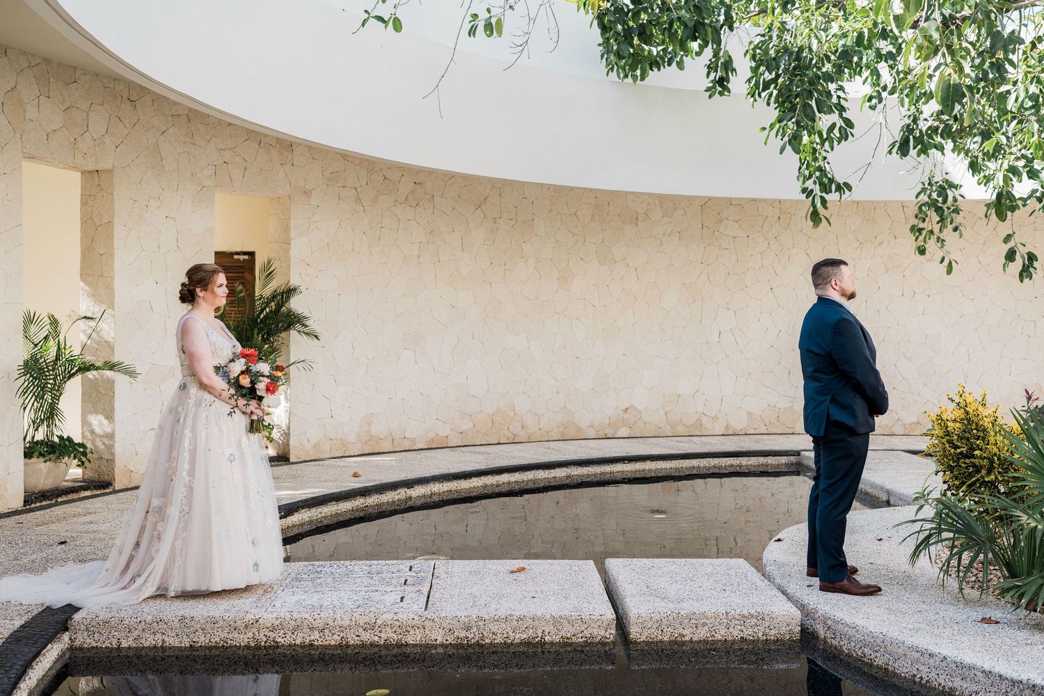 Secrets Akumal Wedding - Bride and groom share first look moment by fountain in elegant outdoor courtyard venue on wedding day.
