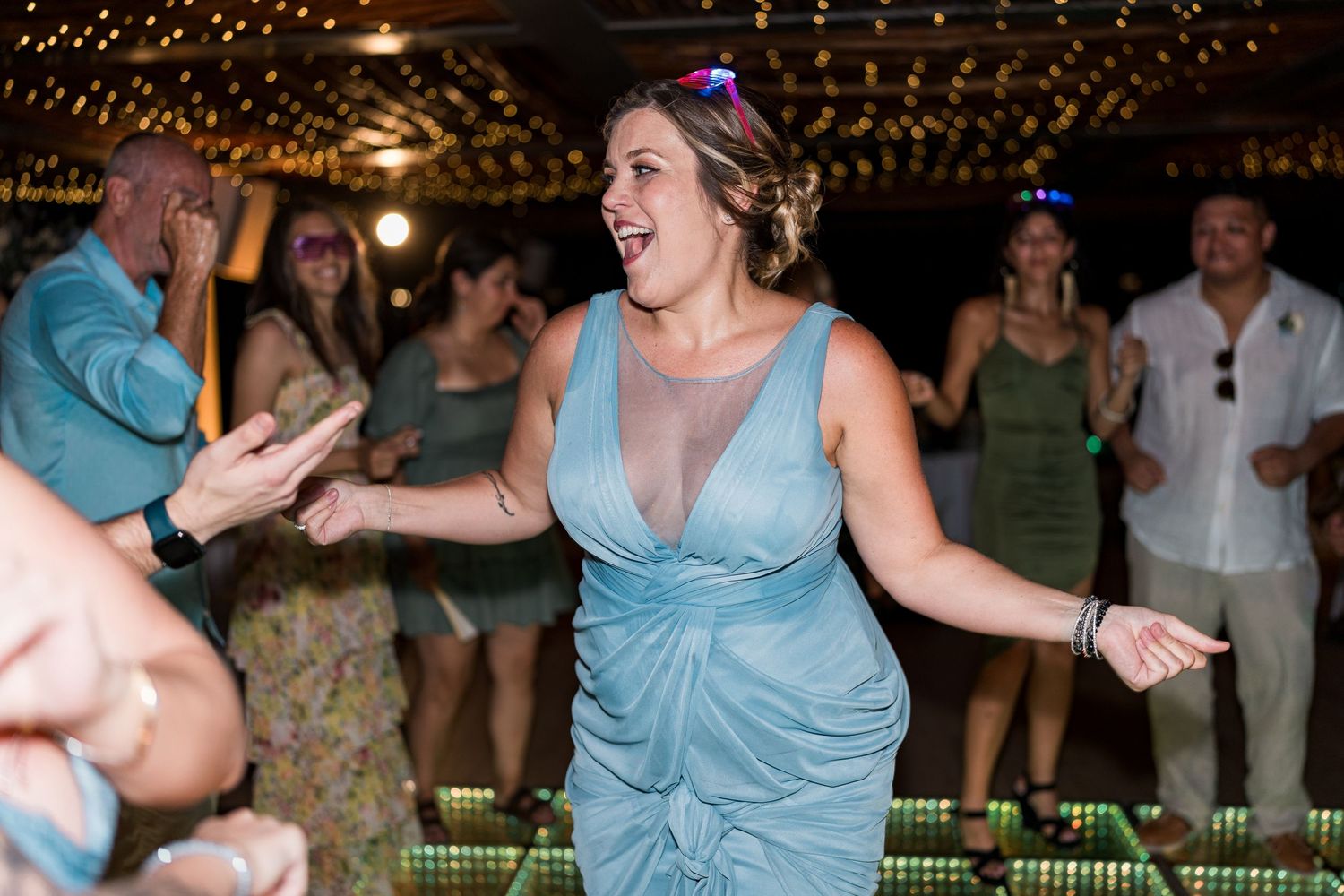 Bridesmaid in blue dress laughing and dancing energetically at an outdoor wedding reception.